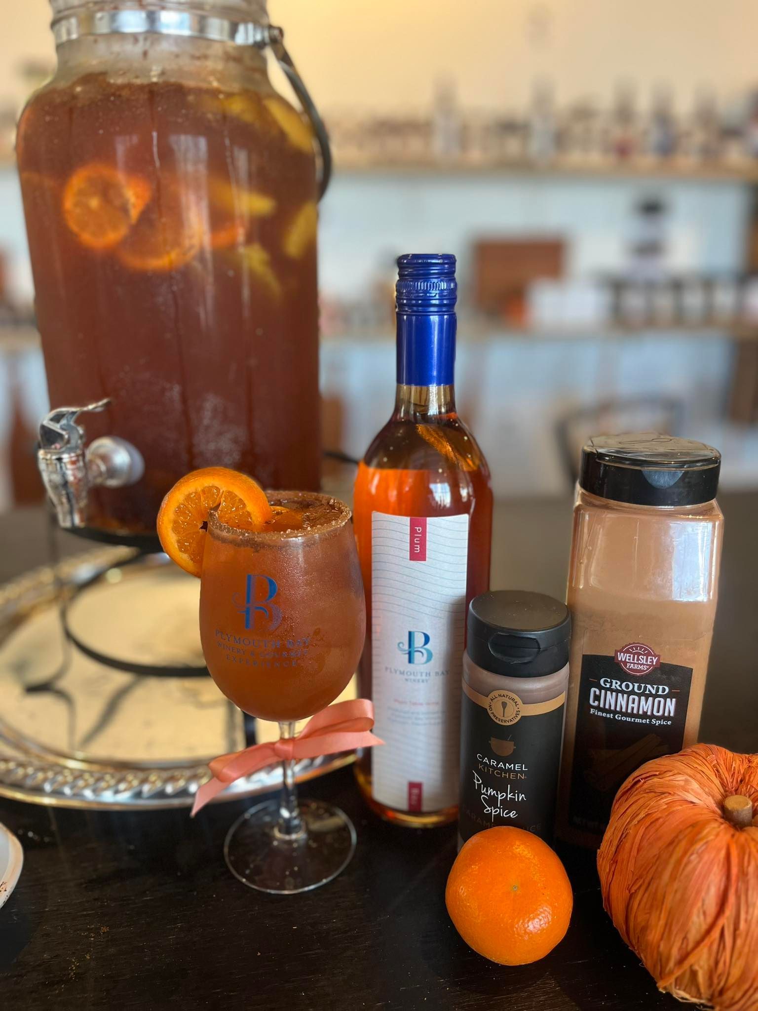 Drink setup: beverage dispenser, wine bottle, spiced rim glass, oranges, pumpkin, cinnamon.