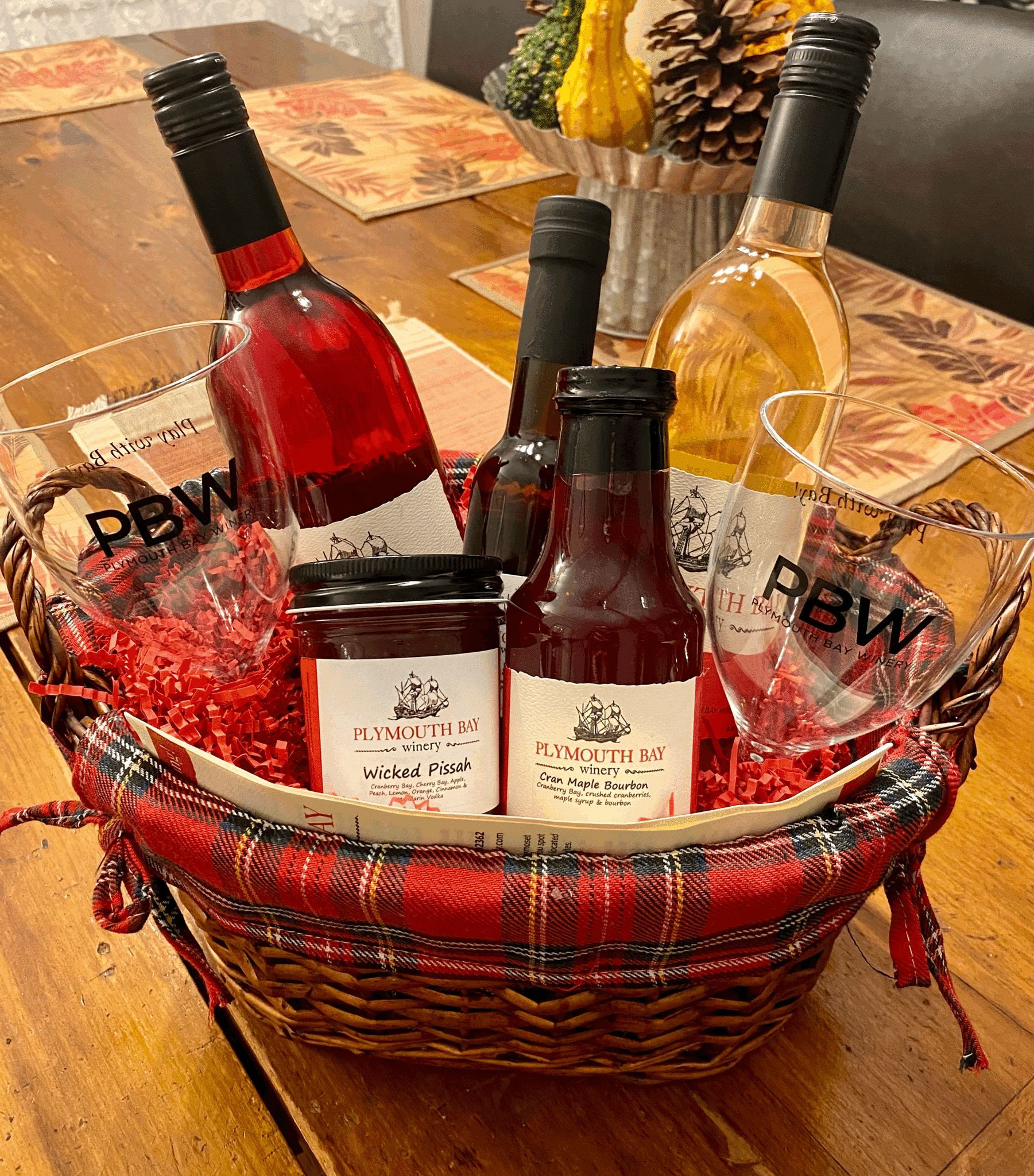 Basket with wine bottles, jam jars, and wine glasses on a wooden table. Red and gold fall decor.