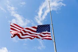 American flag at half-staff, blue sky background.