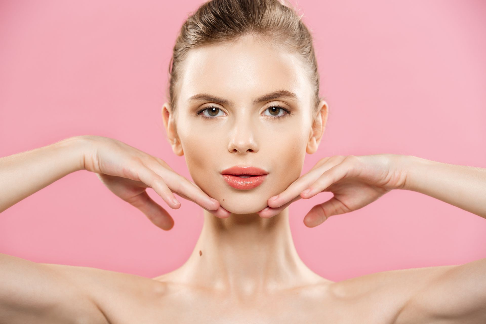 Portrait of a woman with hands framing her face against a pink background