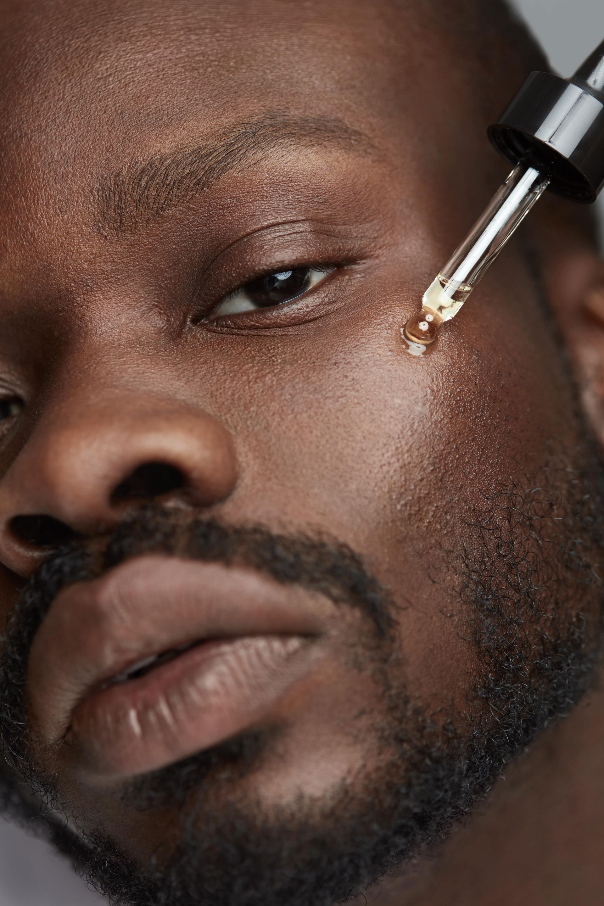 A man with a beard is applying a serum to his face.