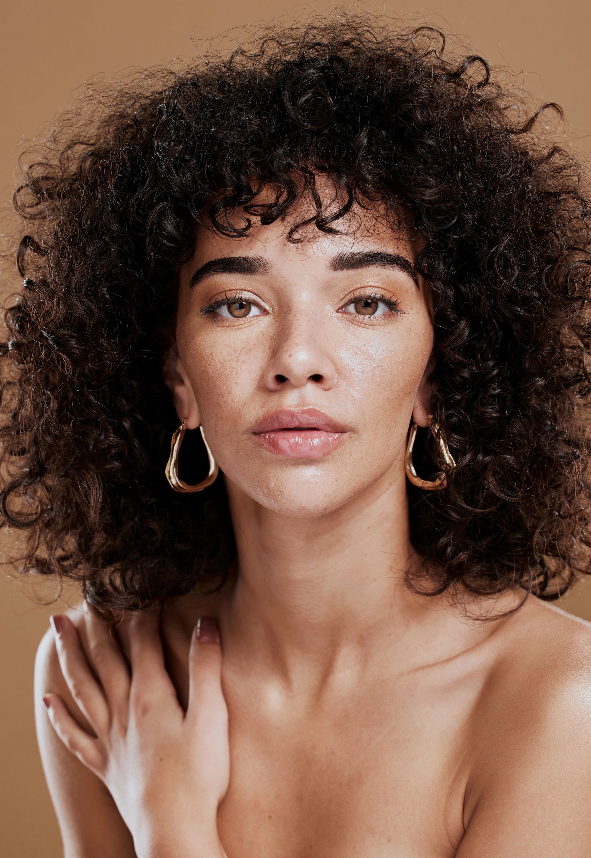 A woman with curly hair is wearing hoop earrings.