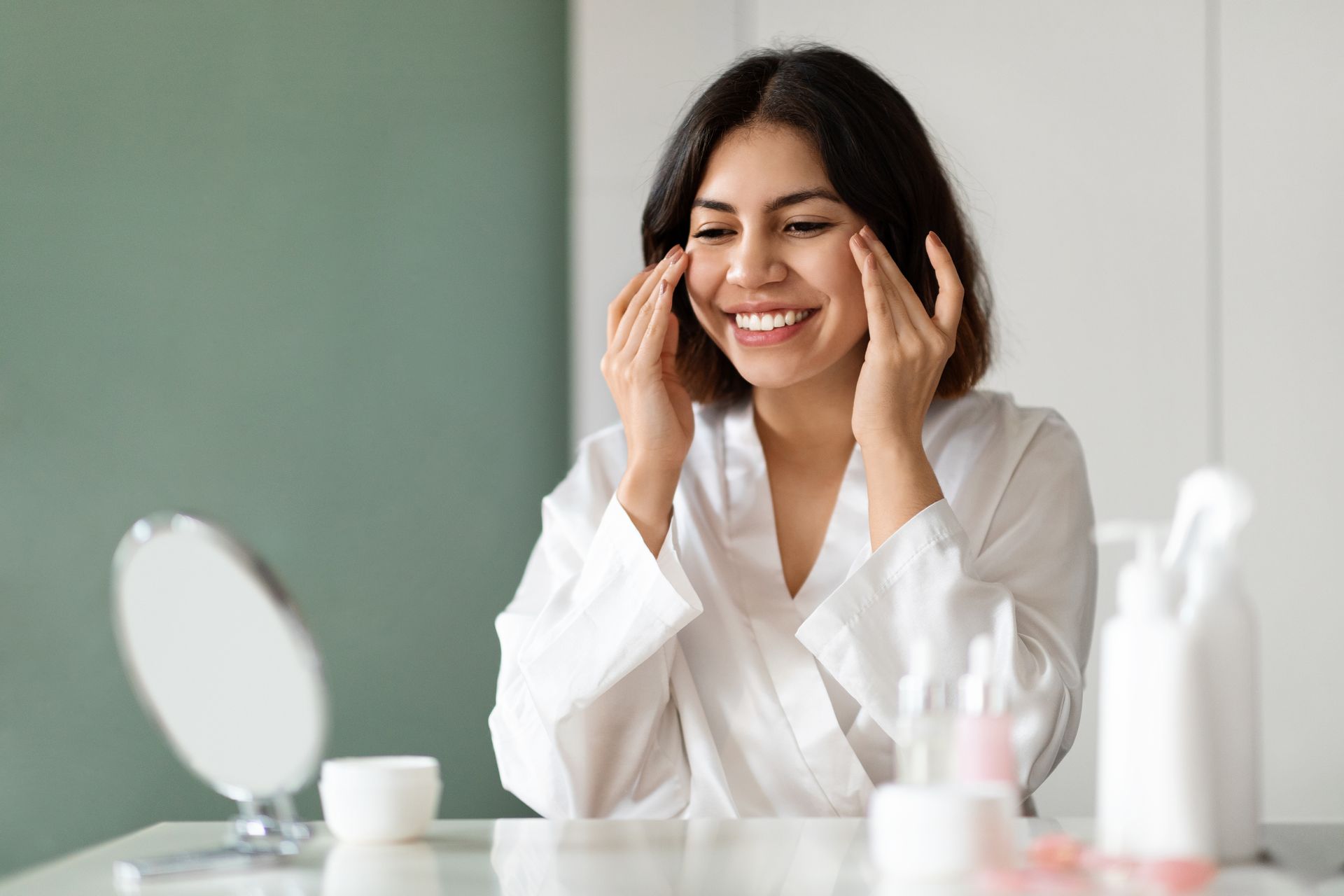 A woman is smiling while looking at her face in a mirror.