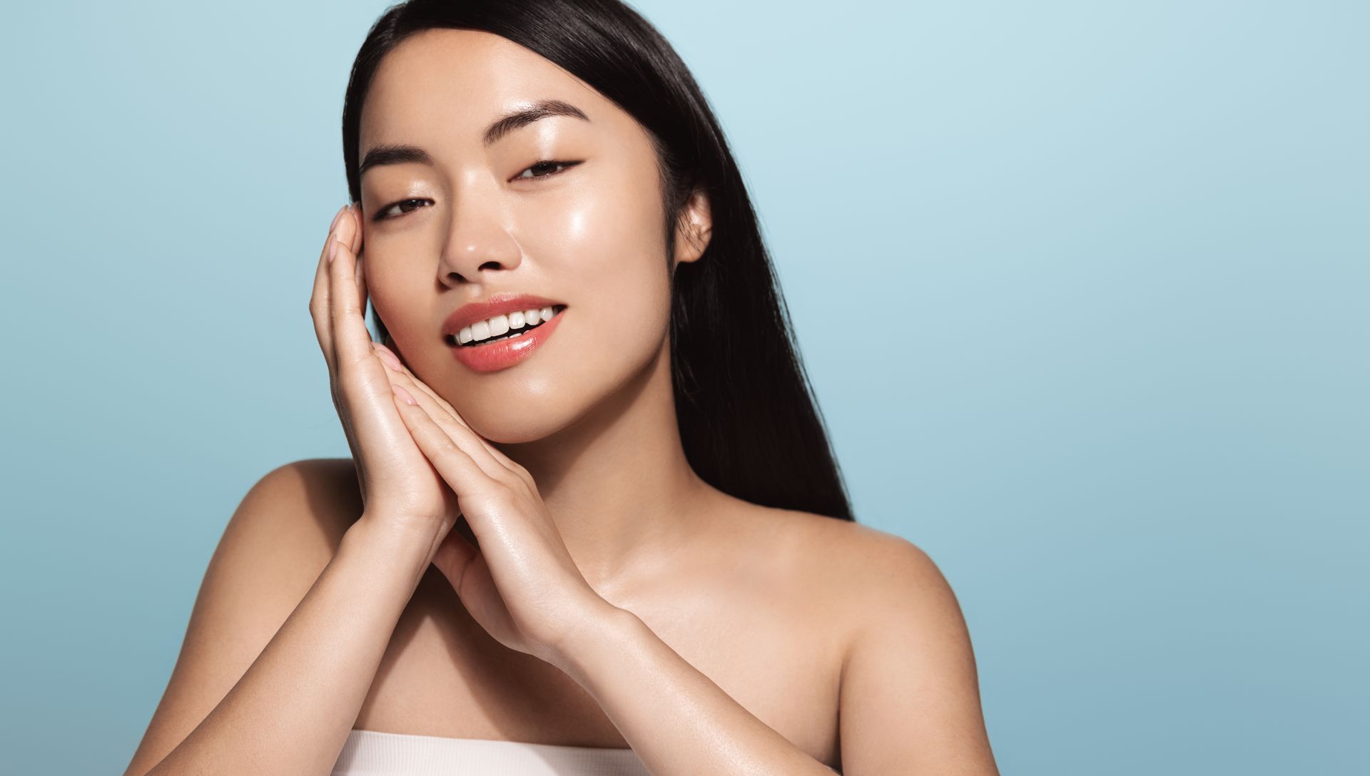 A woman is touching her face with her hands and smiling.