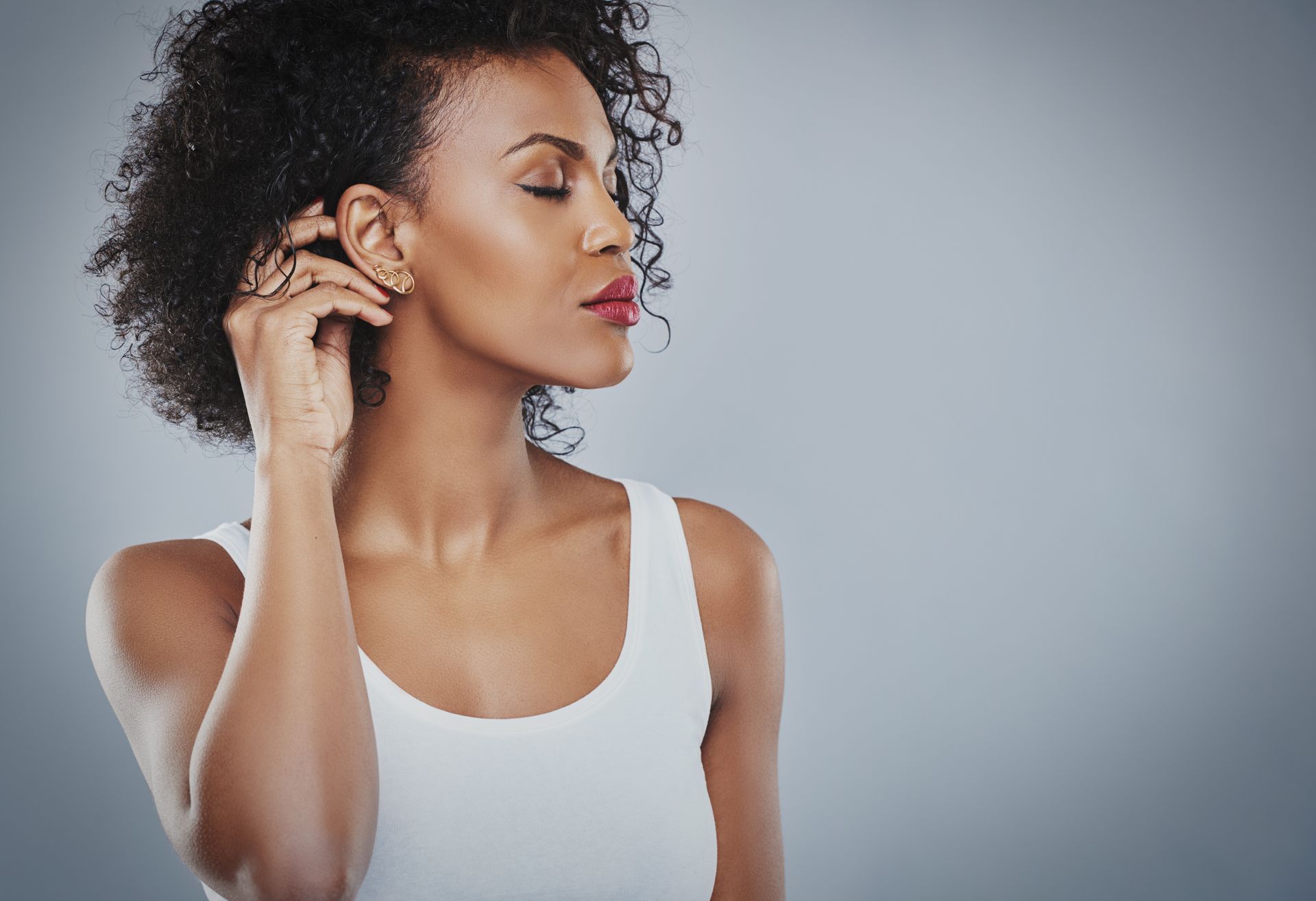 A woman in a white tank top is covering her ear with her hand.
