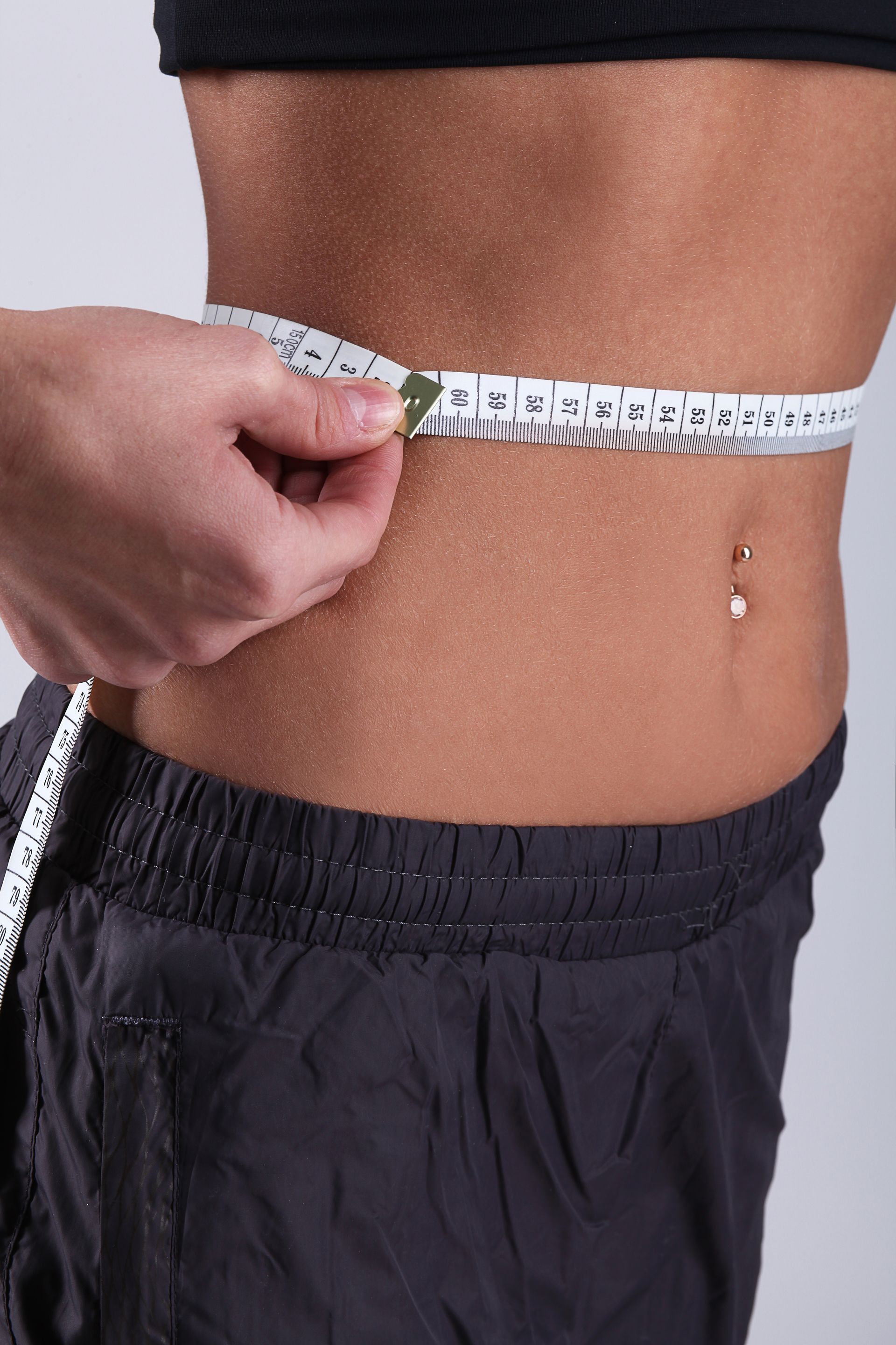 A woman is measuring her waist with a tape measure.