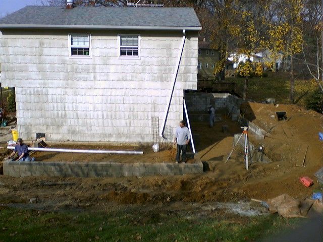 Construction site at the back of a two-story house, workers are building a retaining wall and grading the land.