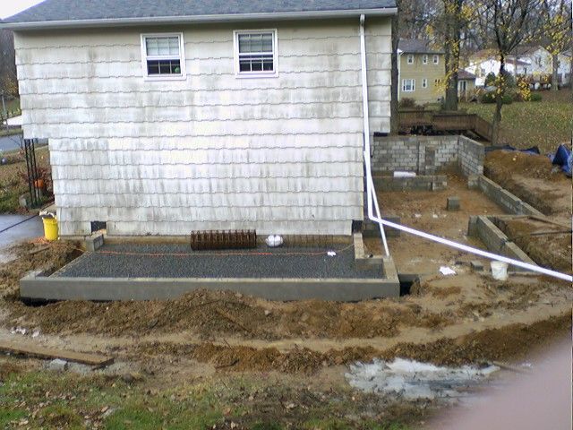 Construction site next to a house. Muddy ground, concrete work, and foundation visible.