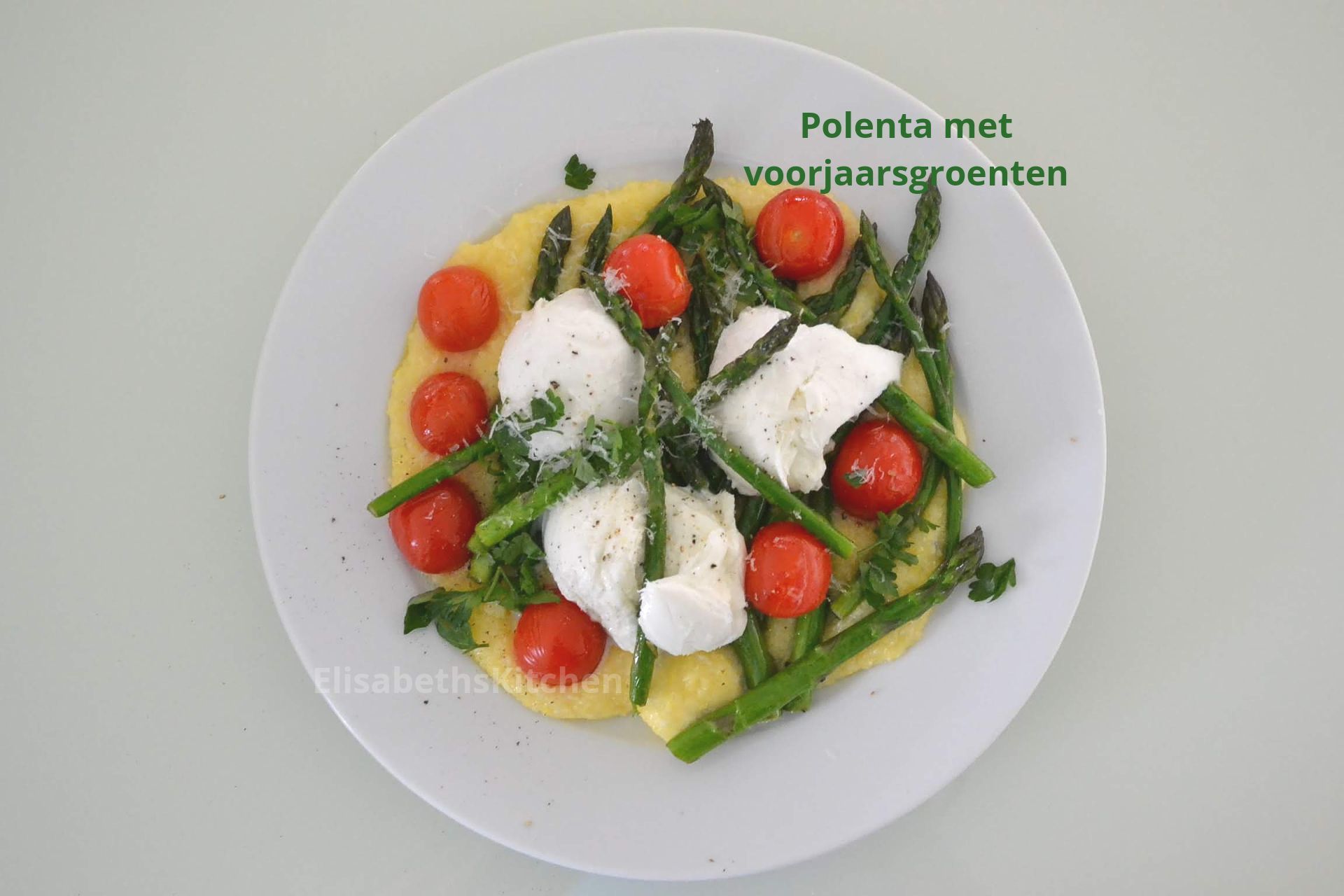 Polenta met asperges, tomaten en gepocheerde eieren op een wit bord. Groene groenten en rode tomaten.