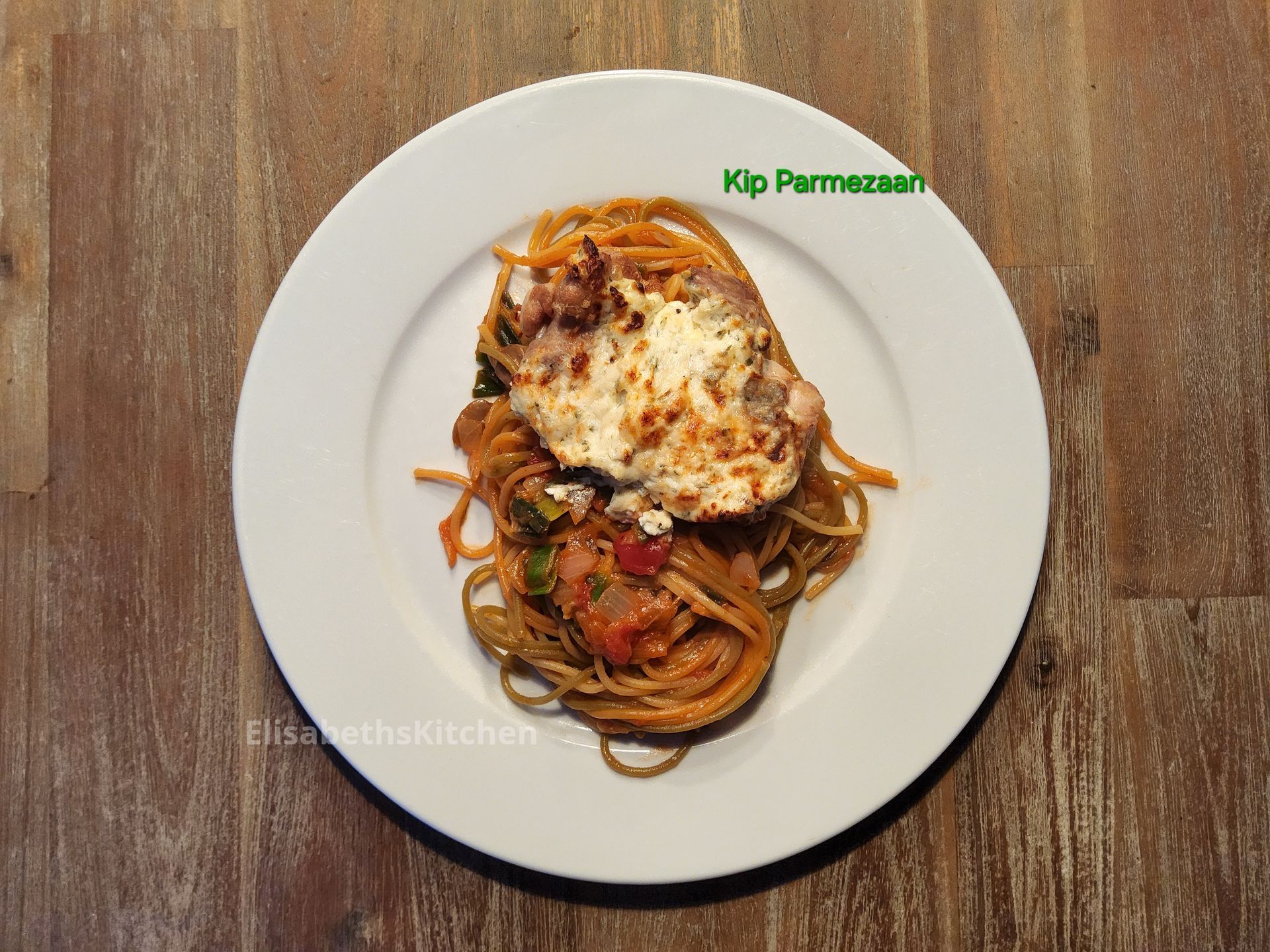 Kip Parmezaan op spaghetti met rode saus, op een wit bord op een houten tafel.