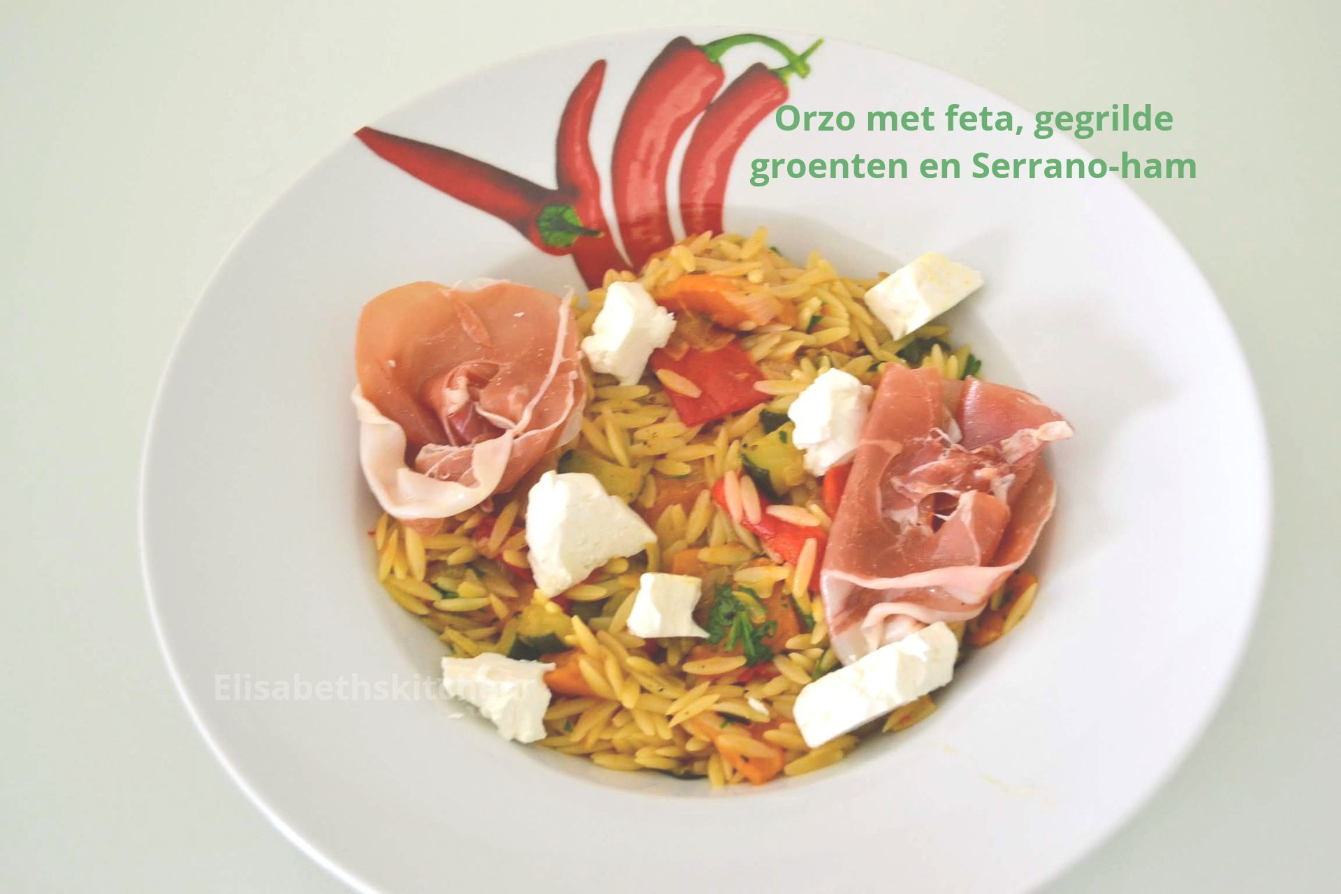 Scroll verder voor het recept Orzosalade met feta, gegrilde groenten en serranoham op een wit bord.