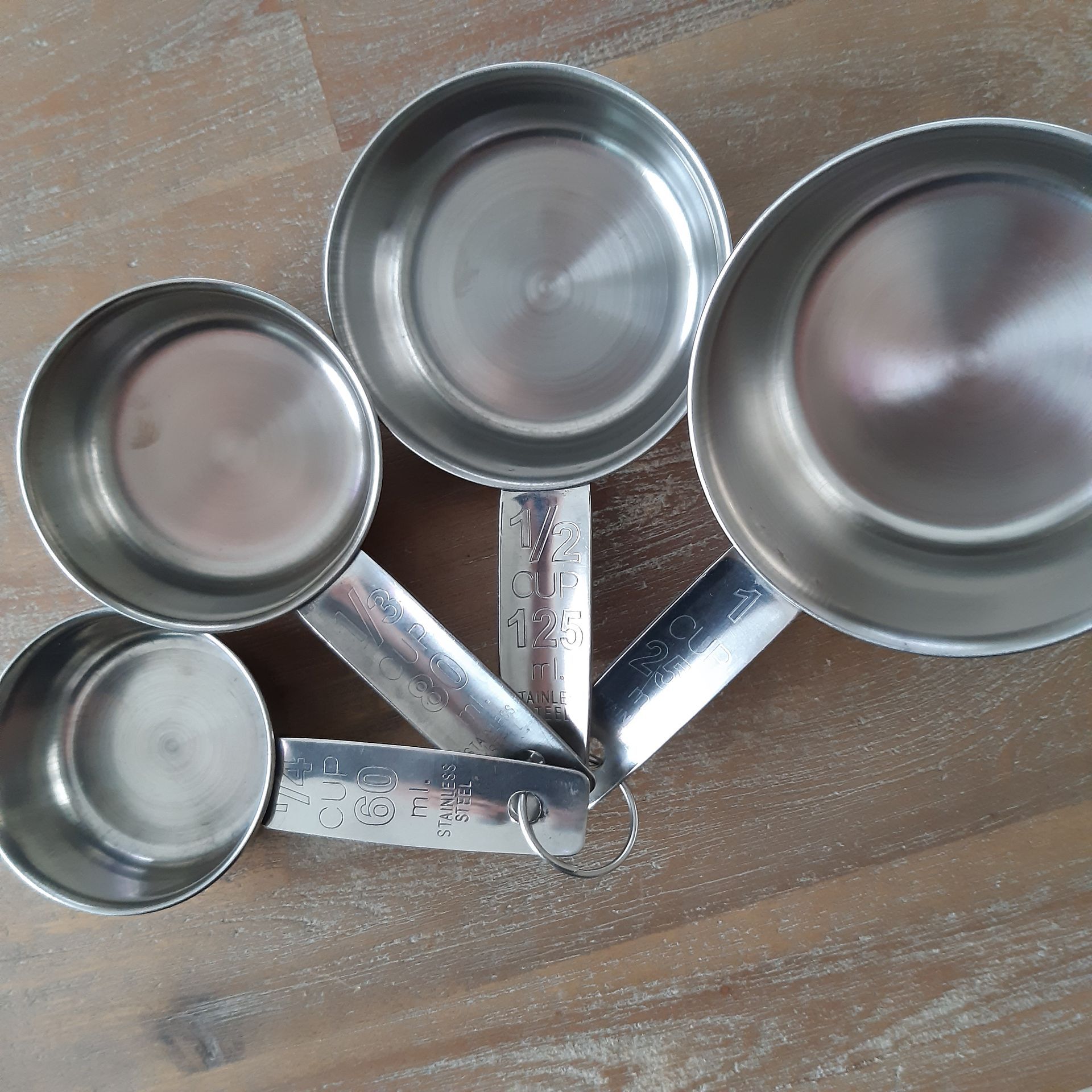 Vier roestvrijstalen maatbekers, op een houten ondergrond gerangschikt op grootte.