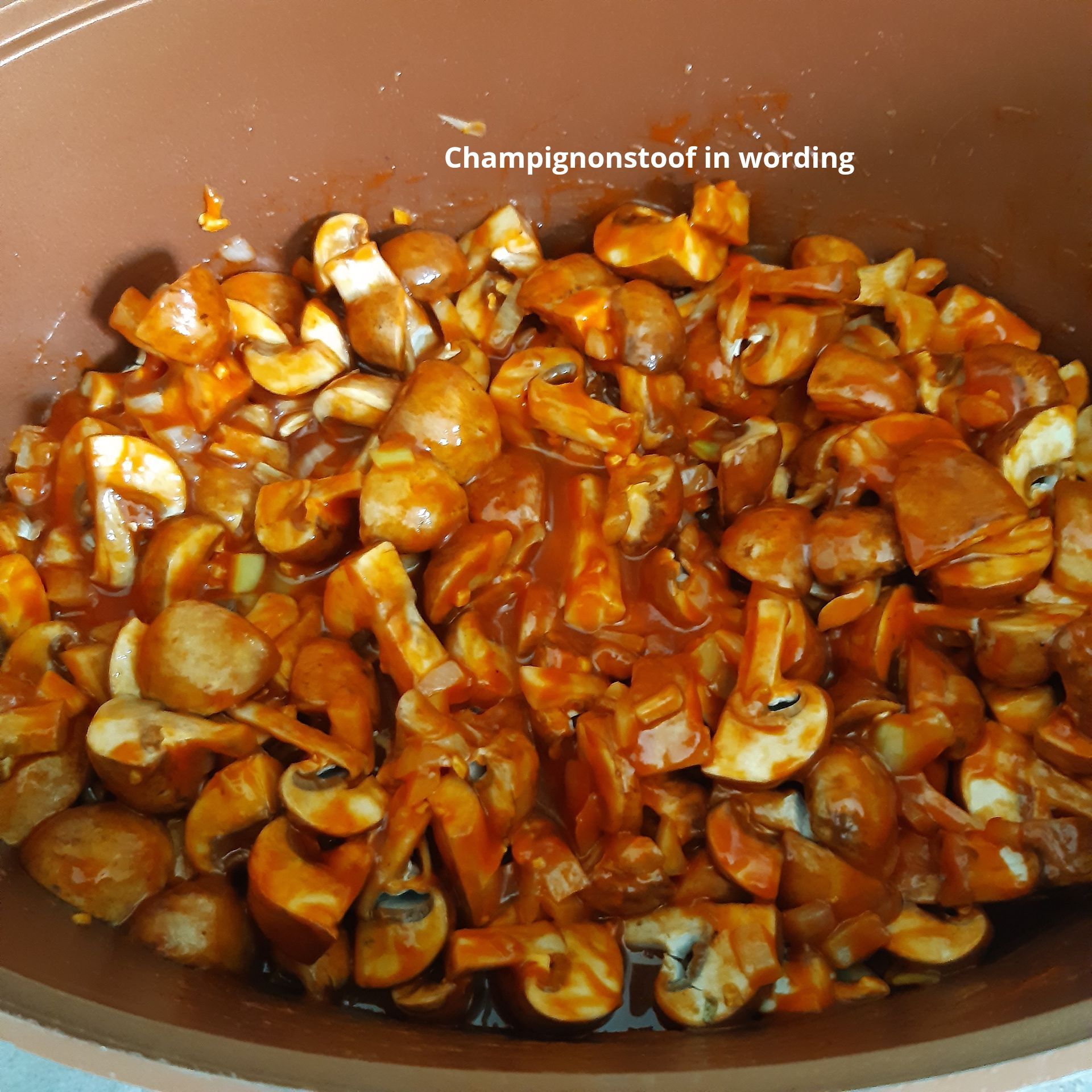 Gehakte champignons gestoofd in een rode saus, in een bruine pan, met de titel