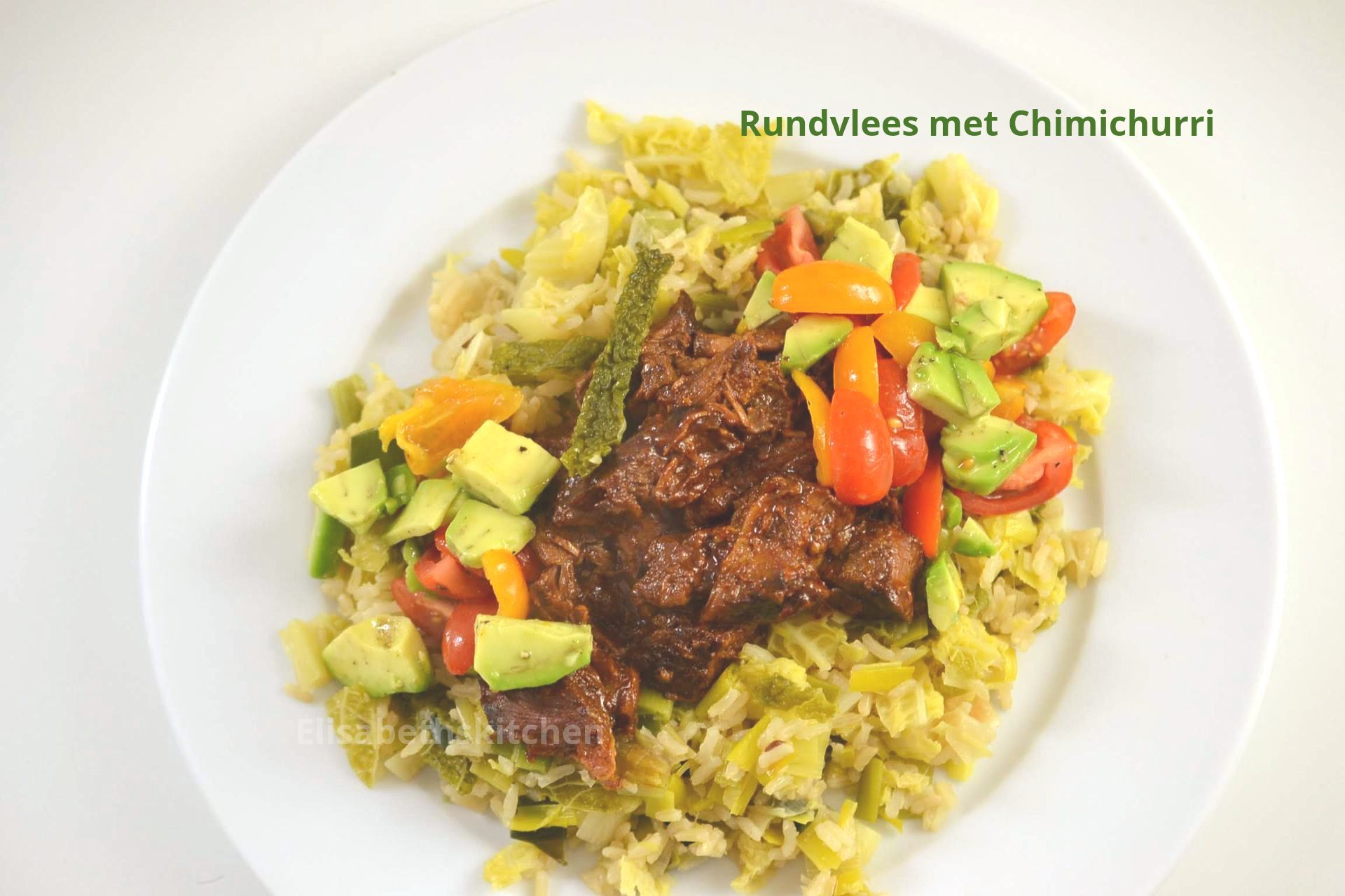 Scroll verder voor het recept Rundvlees met chimichurrisaus op een bedje van groene salade, gegarneerd met avocado en tomaten op een wit bord.
