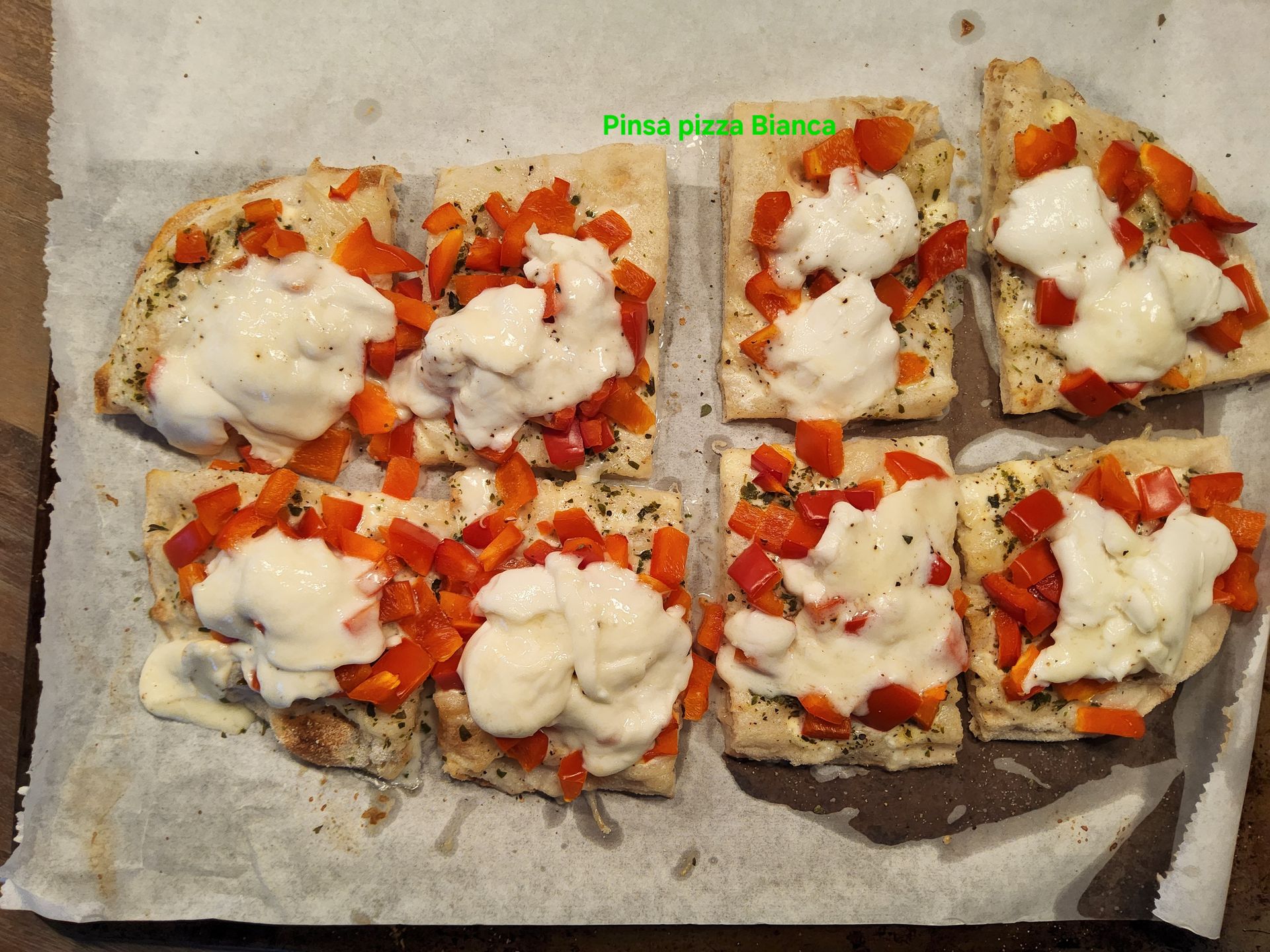 Pizzastukjes met rode paprika en witte kaas, bestrooid met kruiden.