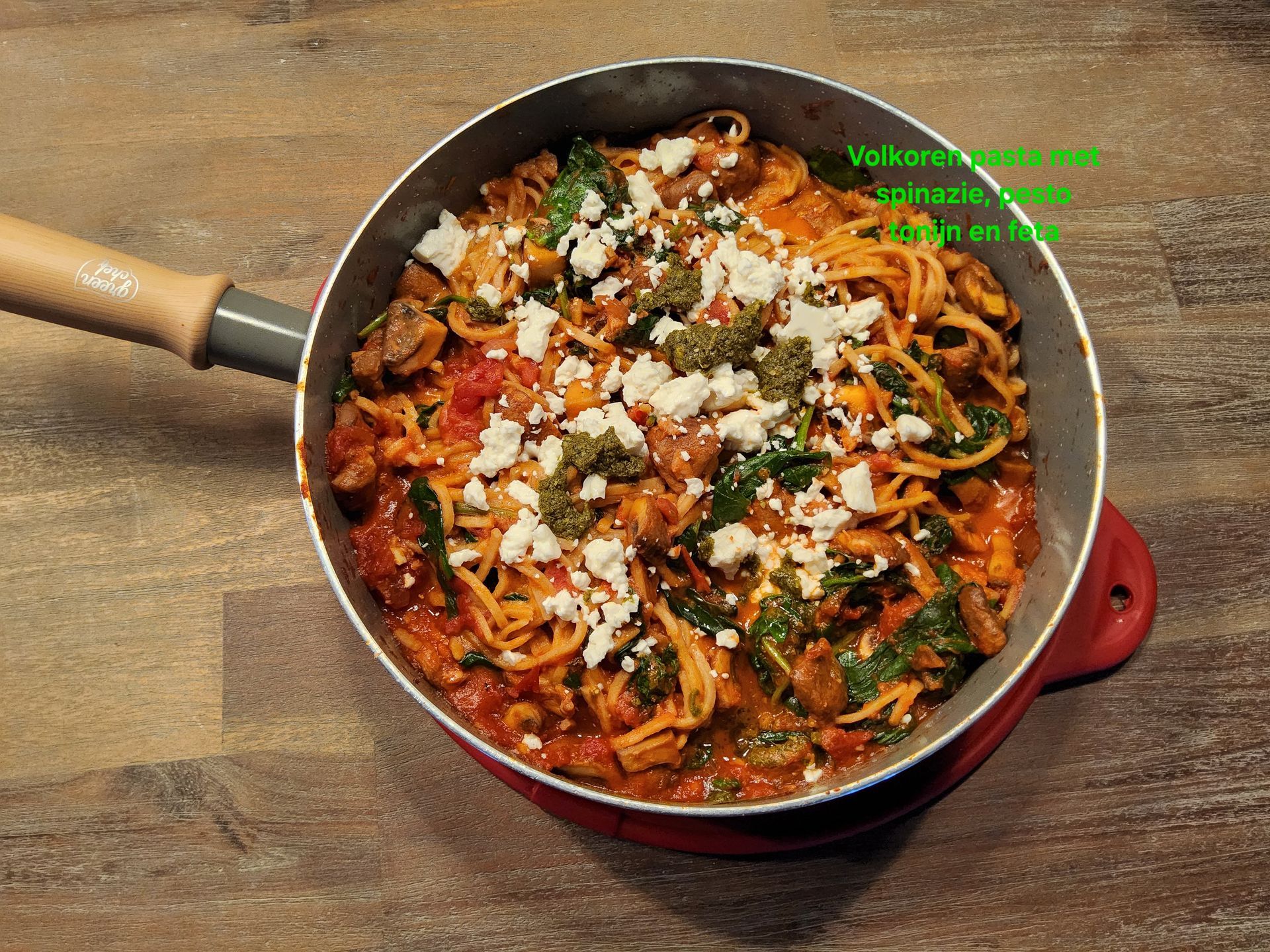 Pastagerecht in een pan, bedekt met kaas en spinazie, op een houten ondergrond.