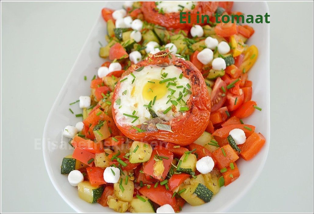 Gebakken tomaten met eieren, mozzarella en gesneden groenten op een wit bord.
