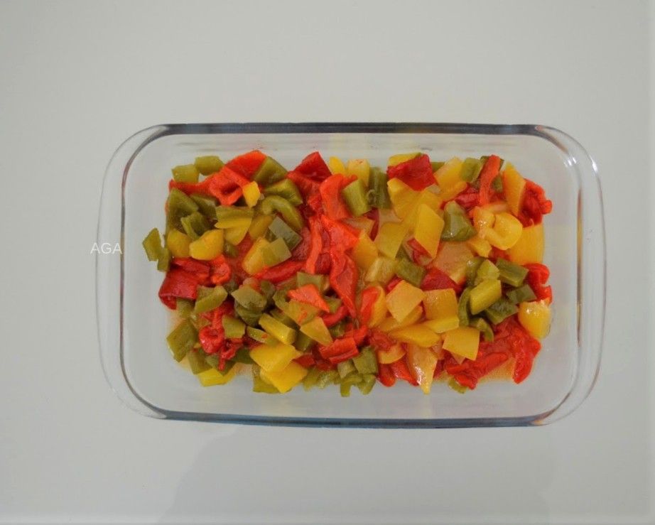 Gesneden rode, gele en groene paprika's in een glazen schaal op een witte ondergrond.