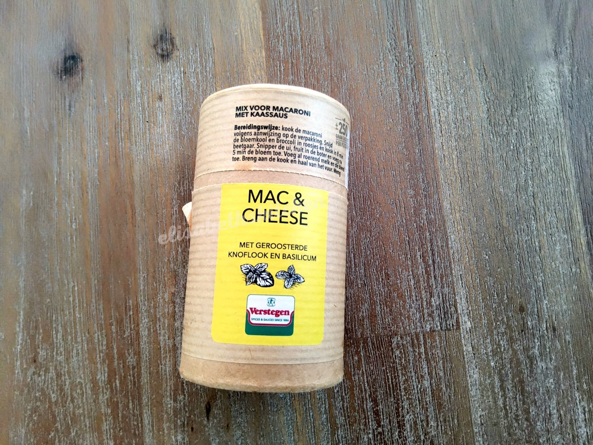 Een cilindervormige bak met macaroni en kaas op een houten ondergrond.