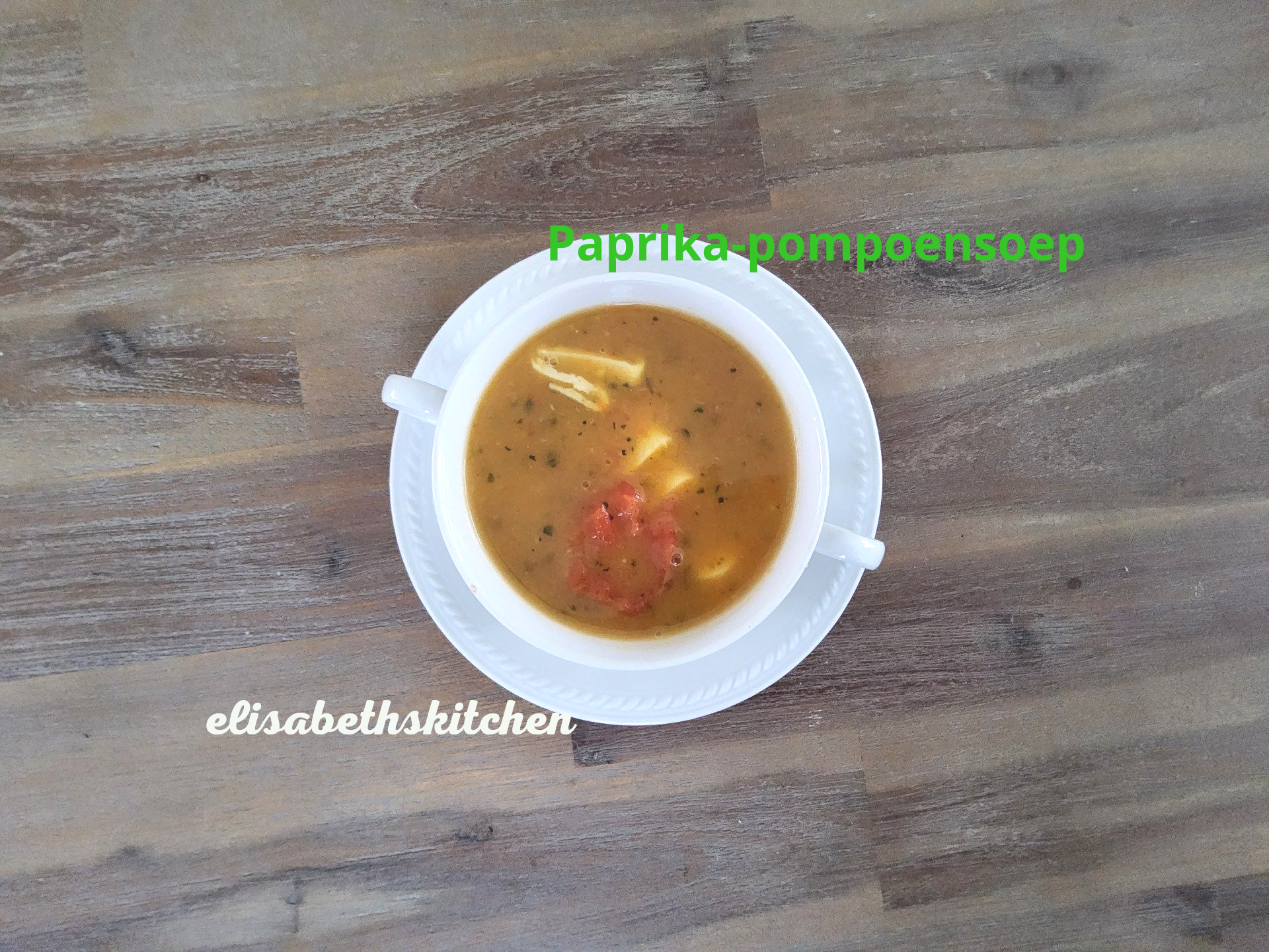Verderop de pagina staat het recept Paprika-pompoensoep in een witte kom op een houten ondergrond.