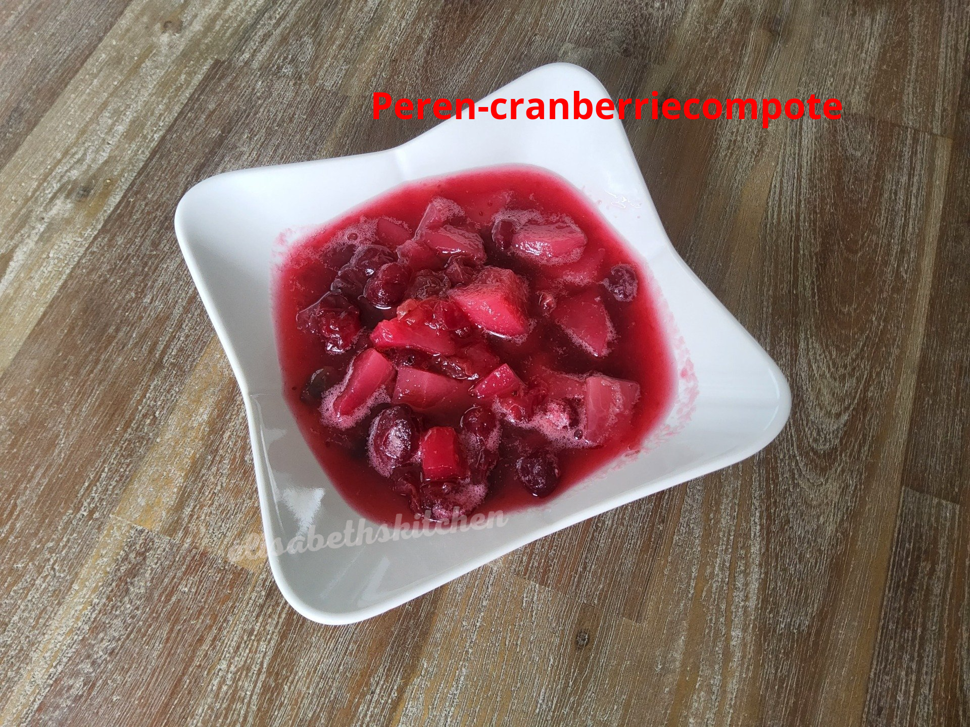 Feron-veenbessencompote in een witte, stervormige kom op een houten ondergrond; rode en roze tinten.