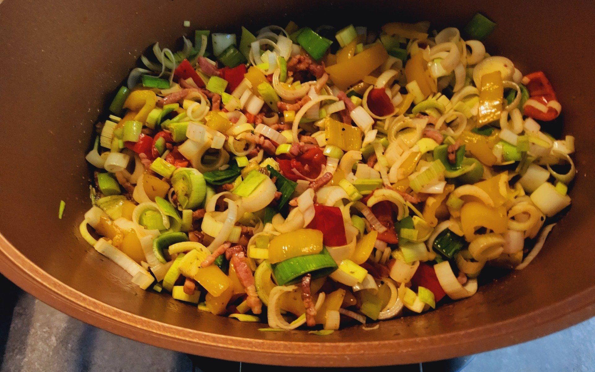 Gekookte groenten in een pan: prei, paprika's en andere ingrediënten, van bovenaf zichtbaar.