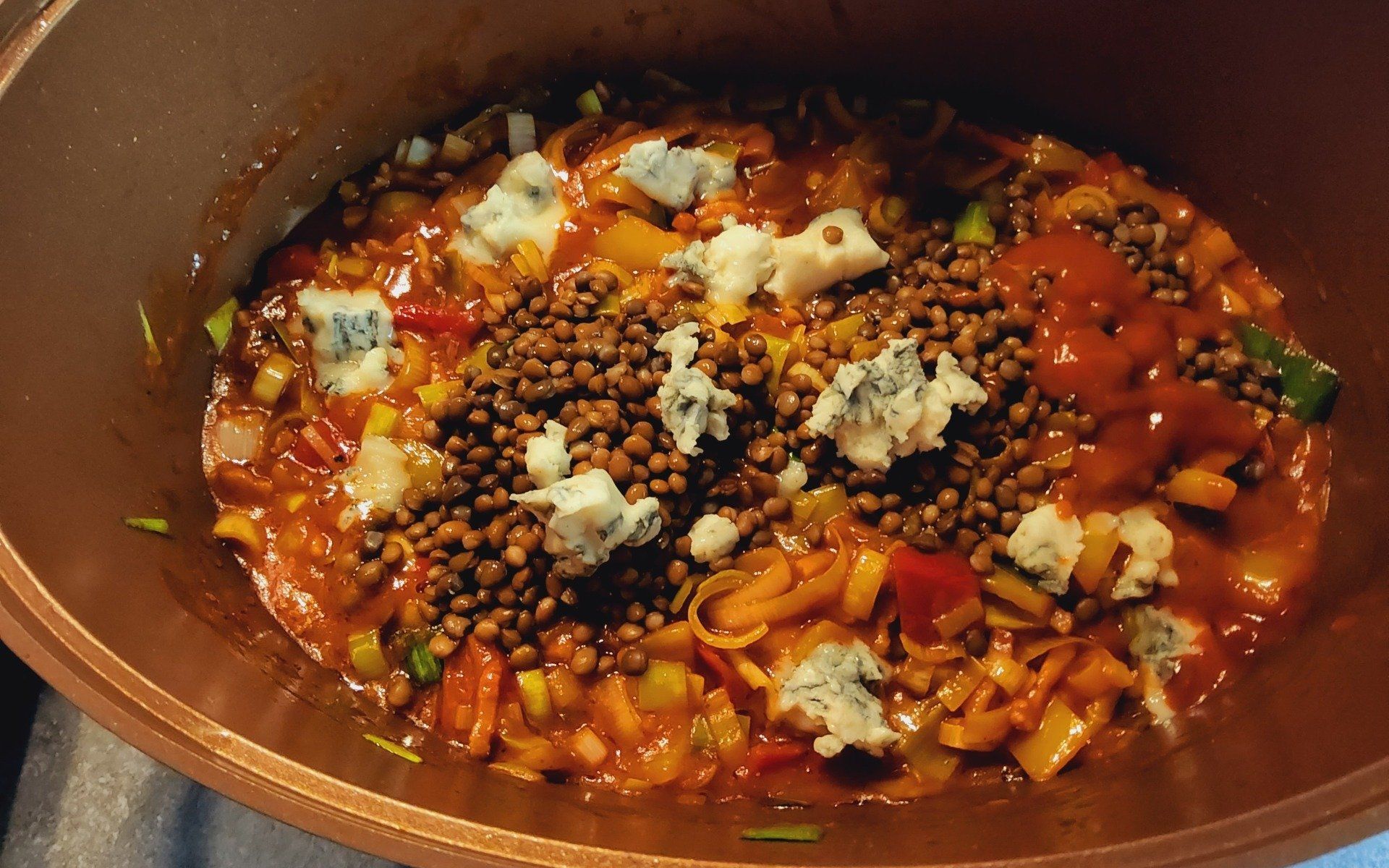 Linzenstoofpot met blauwe kaas in een koperen pot, in oranje en bruine tinten.