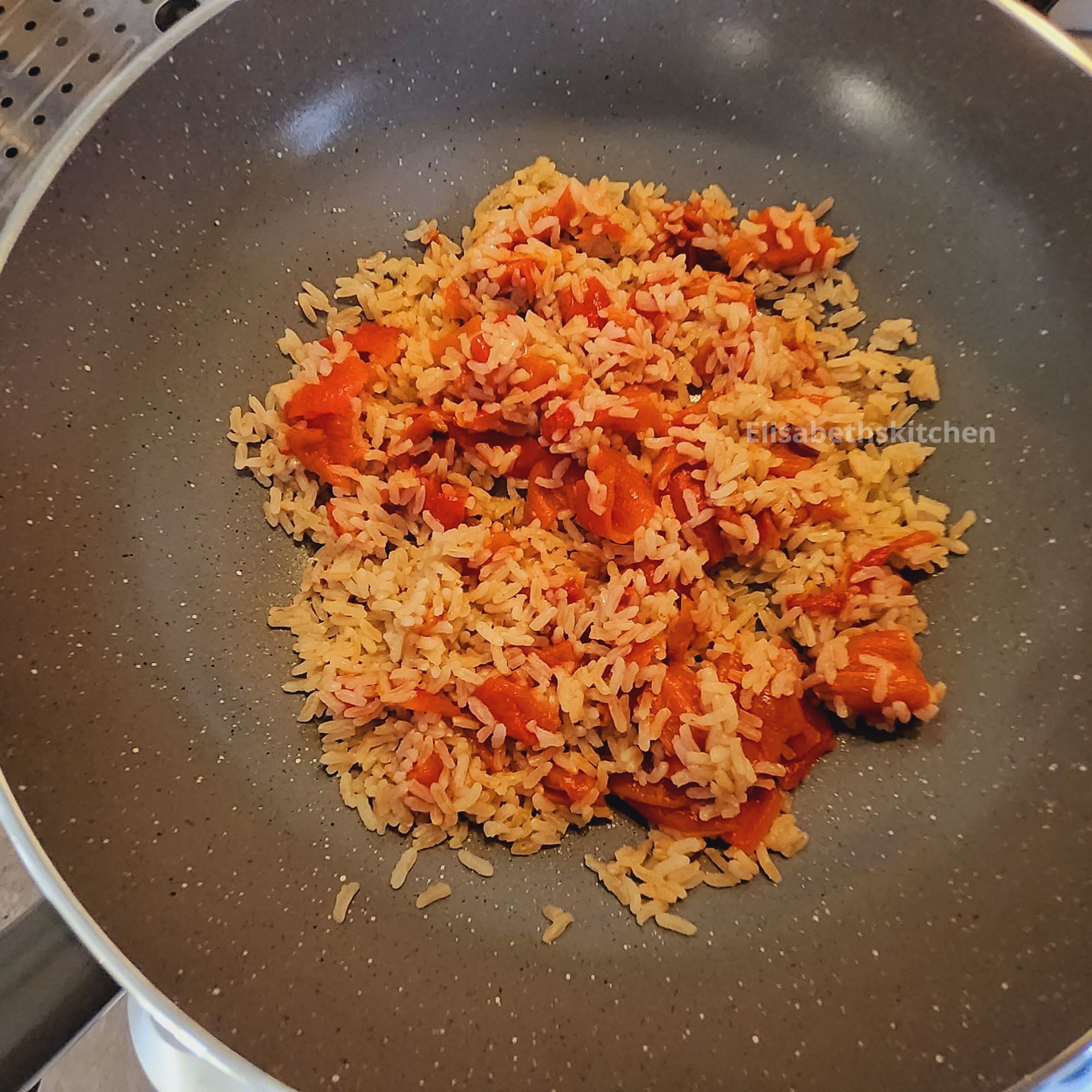 Gekookte rijst met zichtbare stukjes tomaat in een grijze pan.
