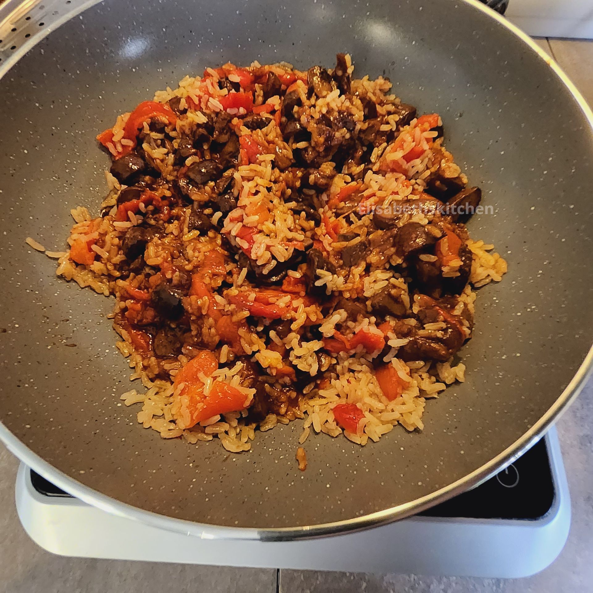Rijstgerecht met groenten, bereid in een grijze wokpan op het fornuis.