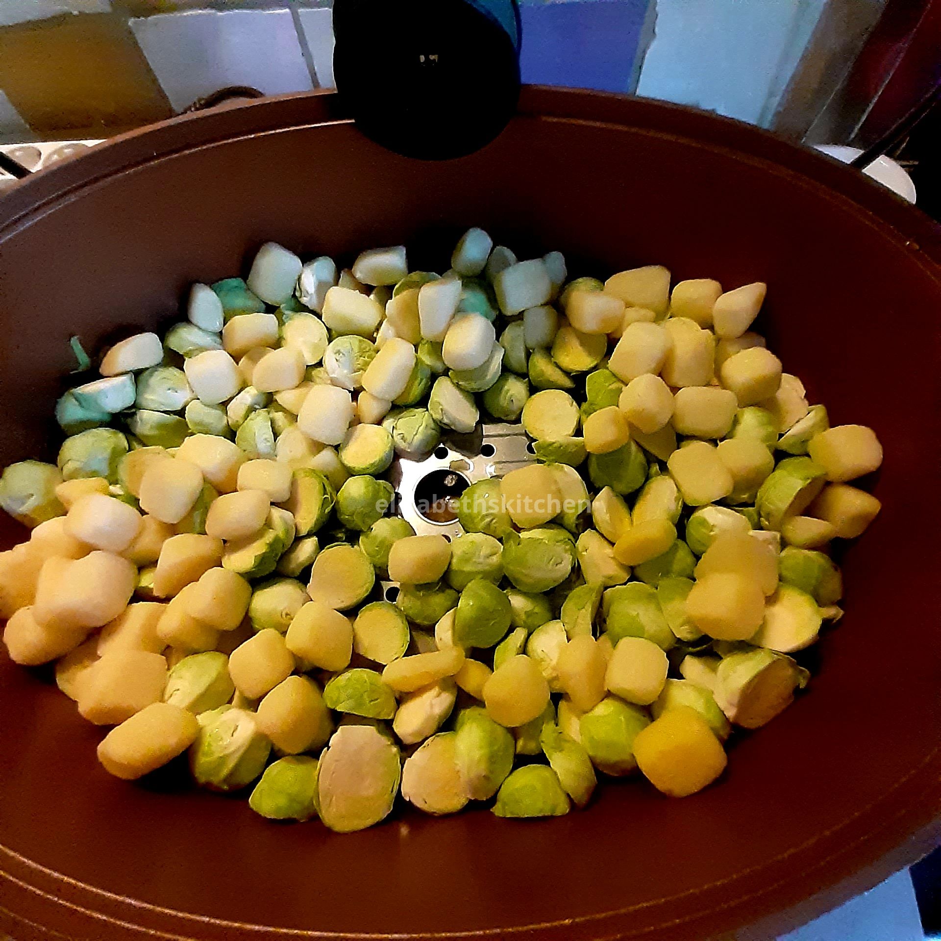 Spruitjes en aardappelen in een bruine kom, klaar om gekookt te worden.