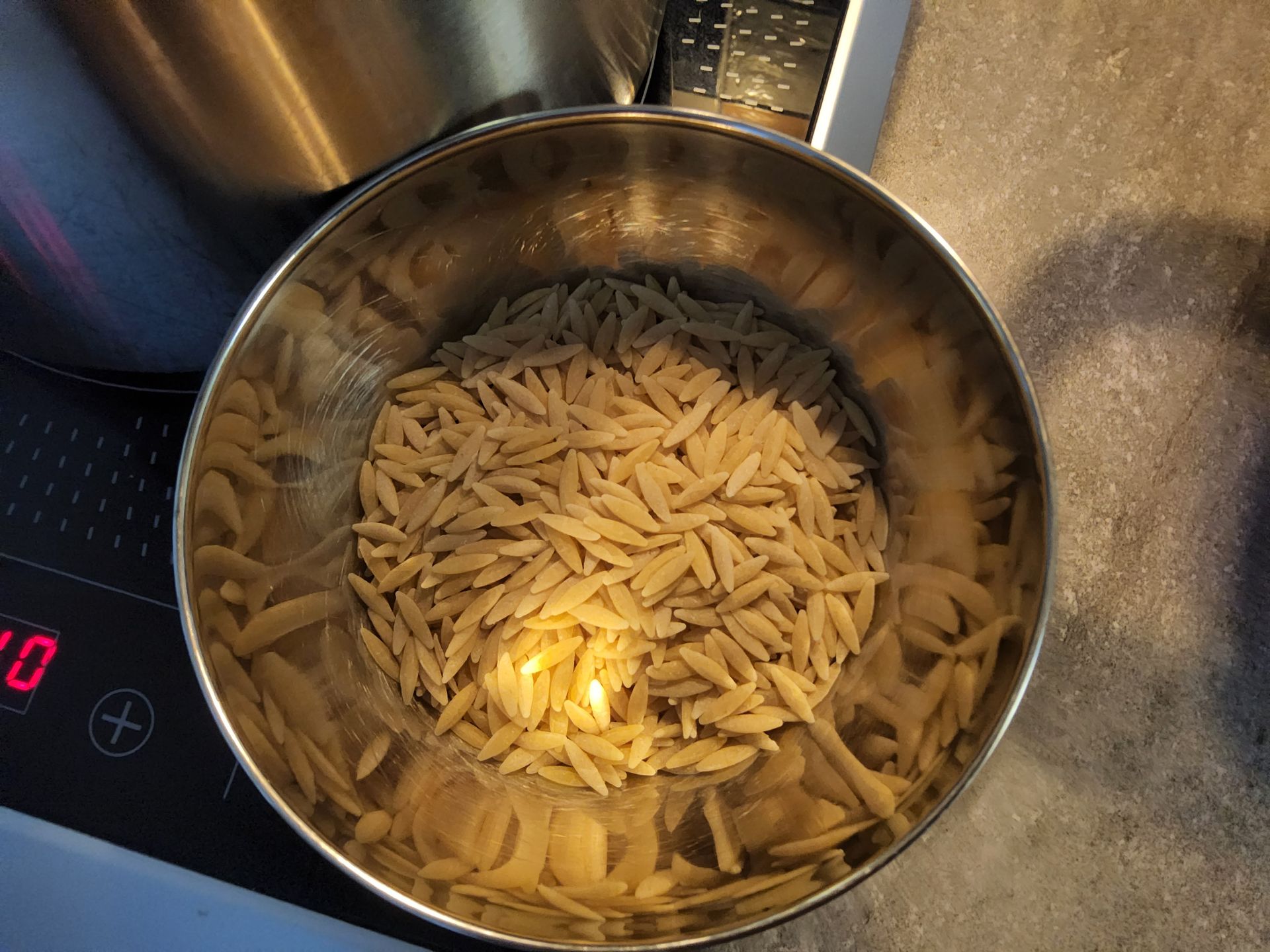 Pasta in een metalen kom, gedeeltelijk ondergedompeld in vloeistof, op een fornuis.