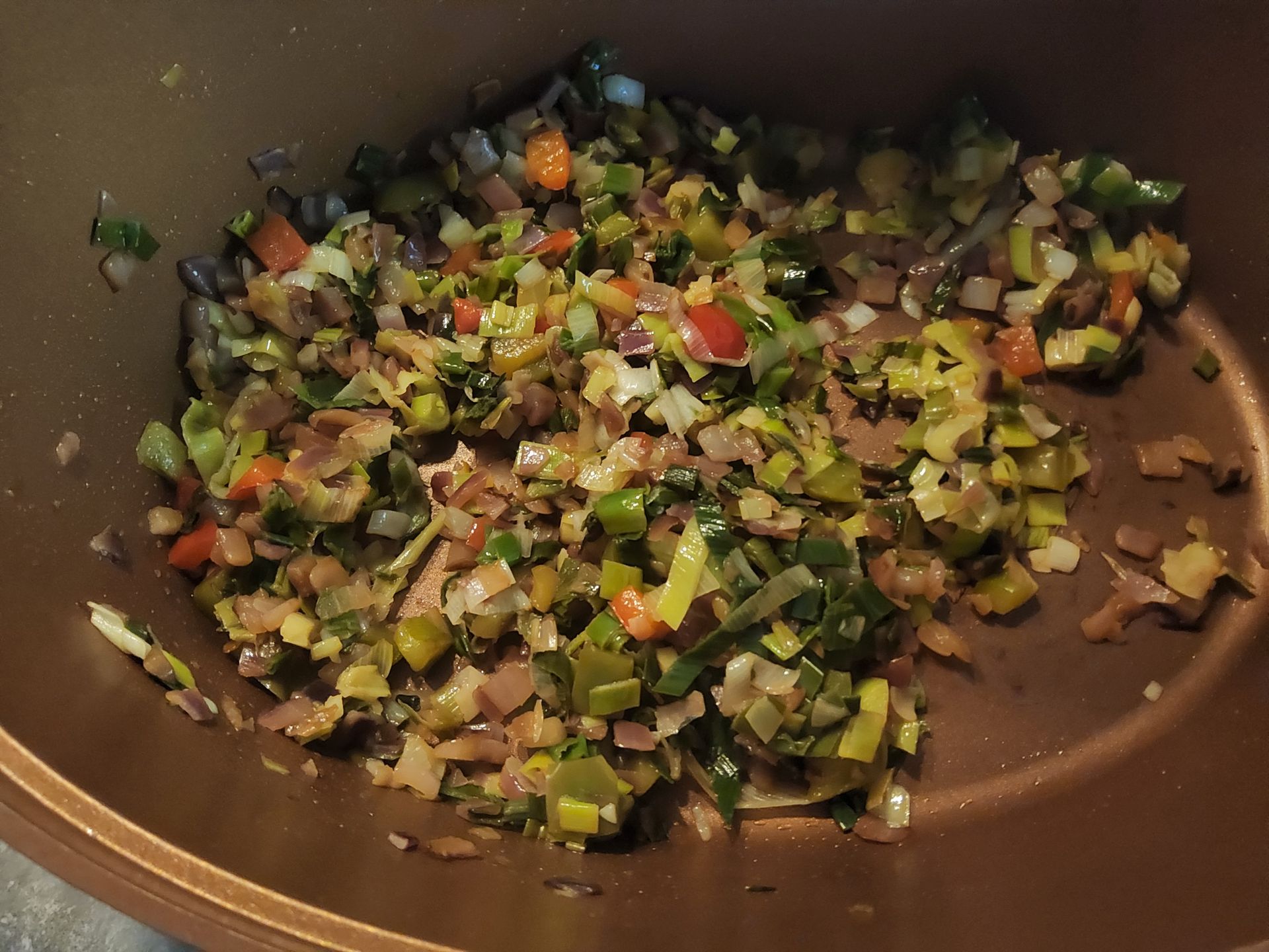 Gesneden groenten (prei, paprika) worden gebakken in een koperkleurige pan.