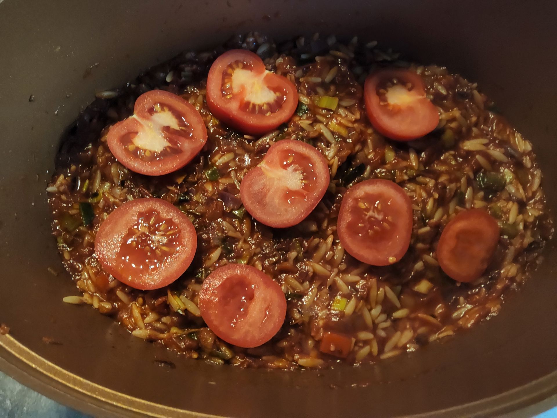 Gekookt rijstgerecht met tomatenschijfjes, gebakken in een bruine pan.
