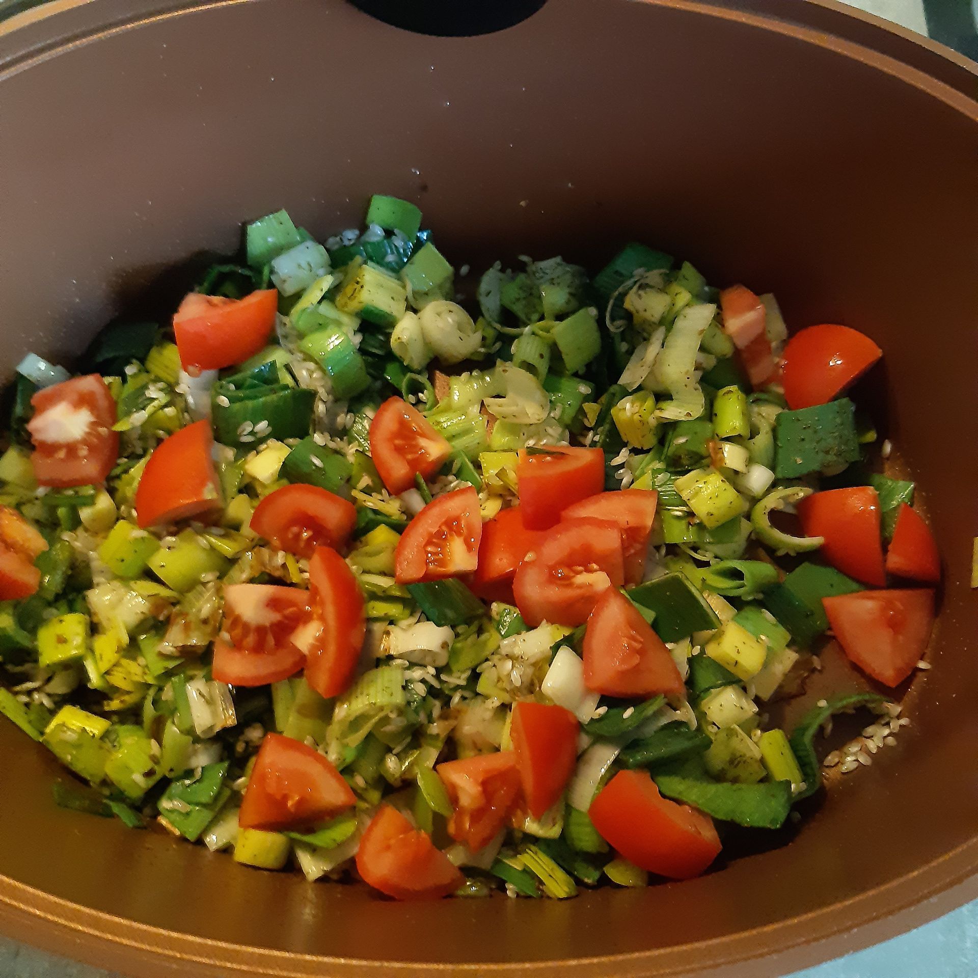 Gesneden groenten, waaronder tomaten en prei, in een bruine kookpot.