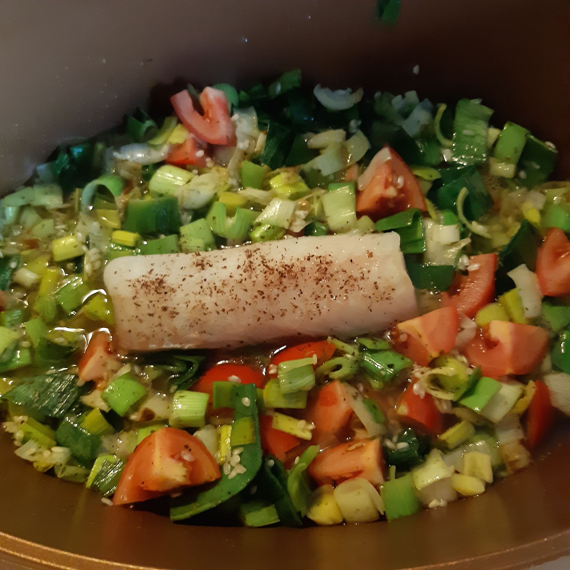 Visfilet met gehakte tomaten, prei en kruiden in een koperen pan.
