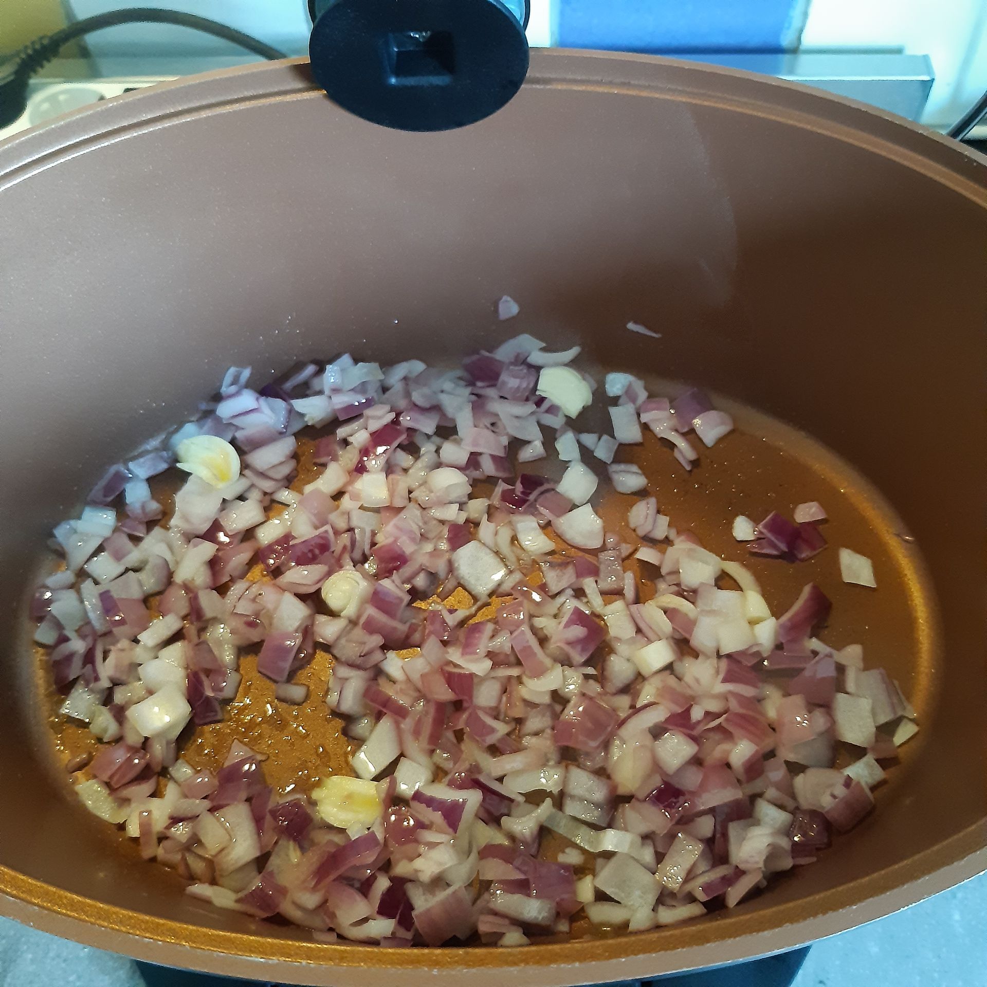 Gesneden rode uien en knoflook worden gekookt in een koperkleurige pan.