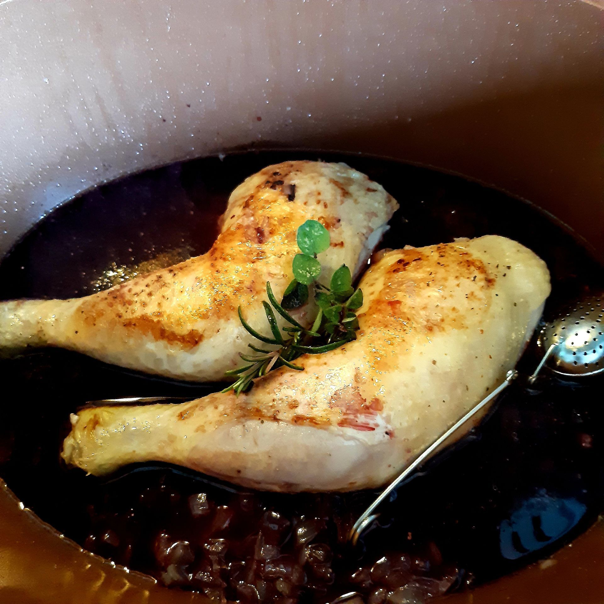 Twee kippenpootjes in een donkere saus met kruiden in een pan.