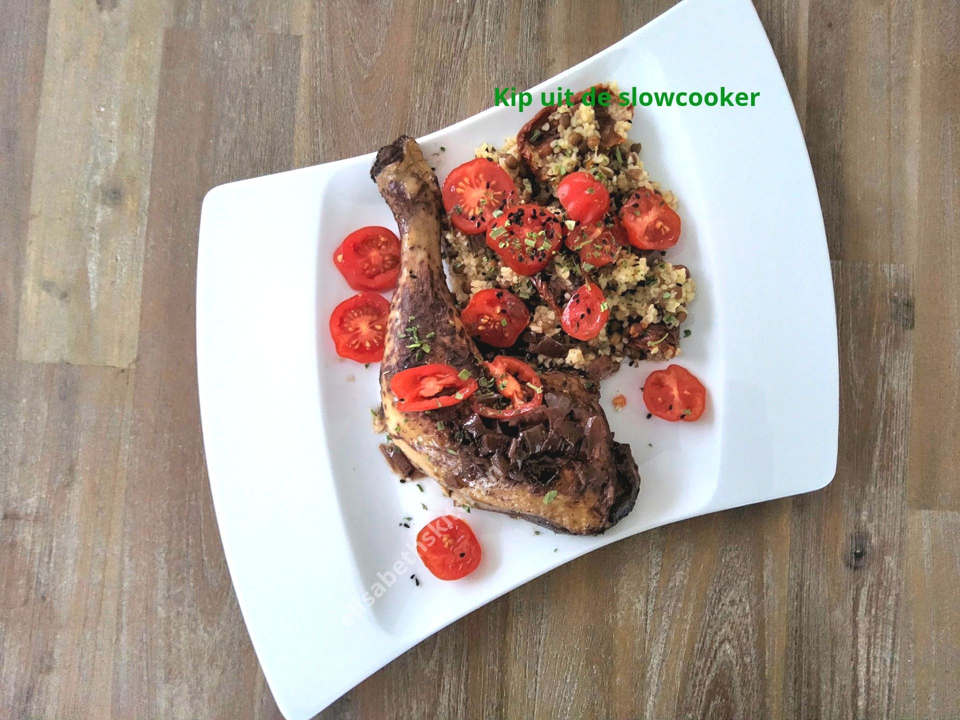 Kippenpoot en quinoa met tomaten op een wit bord, houten tafel.