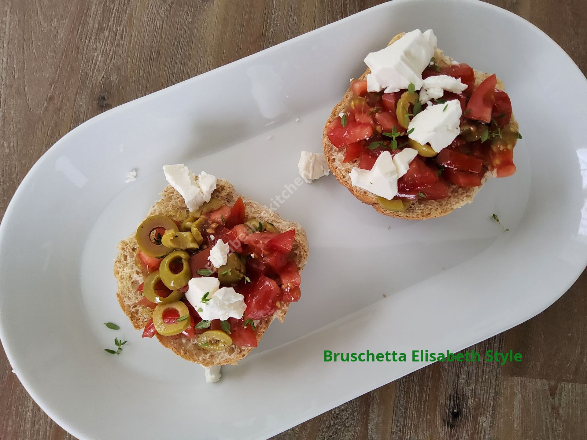 Twee bruschettatoastjes met tomaat, olijven en feta op een wit bord.