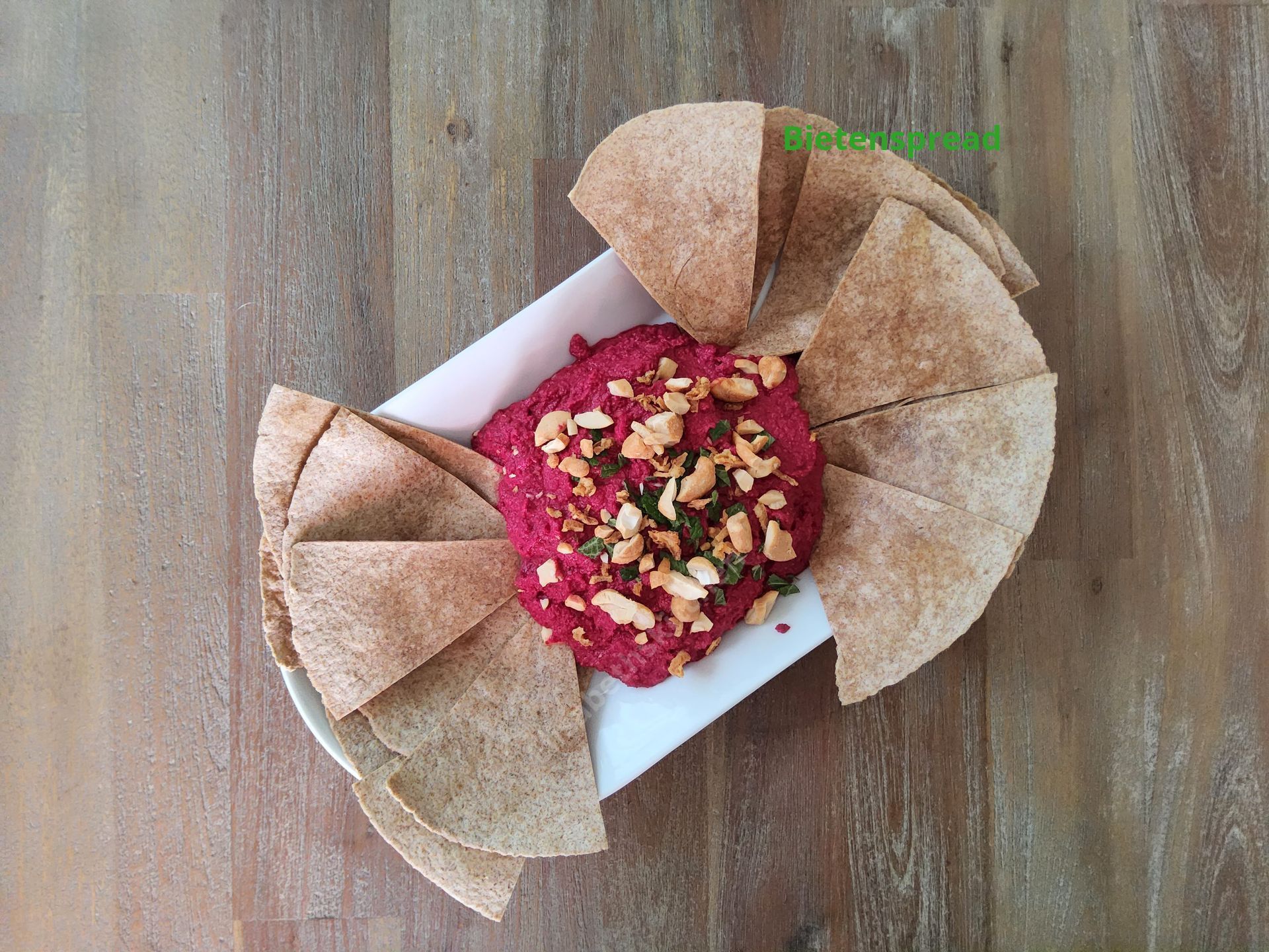 Bietenhummus met geroosterd pitabrood op een wit bord, op een houten tafel.