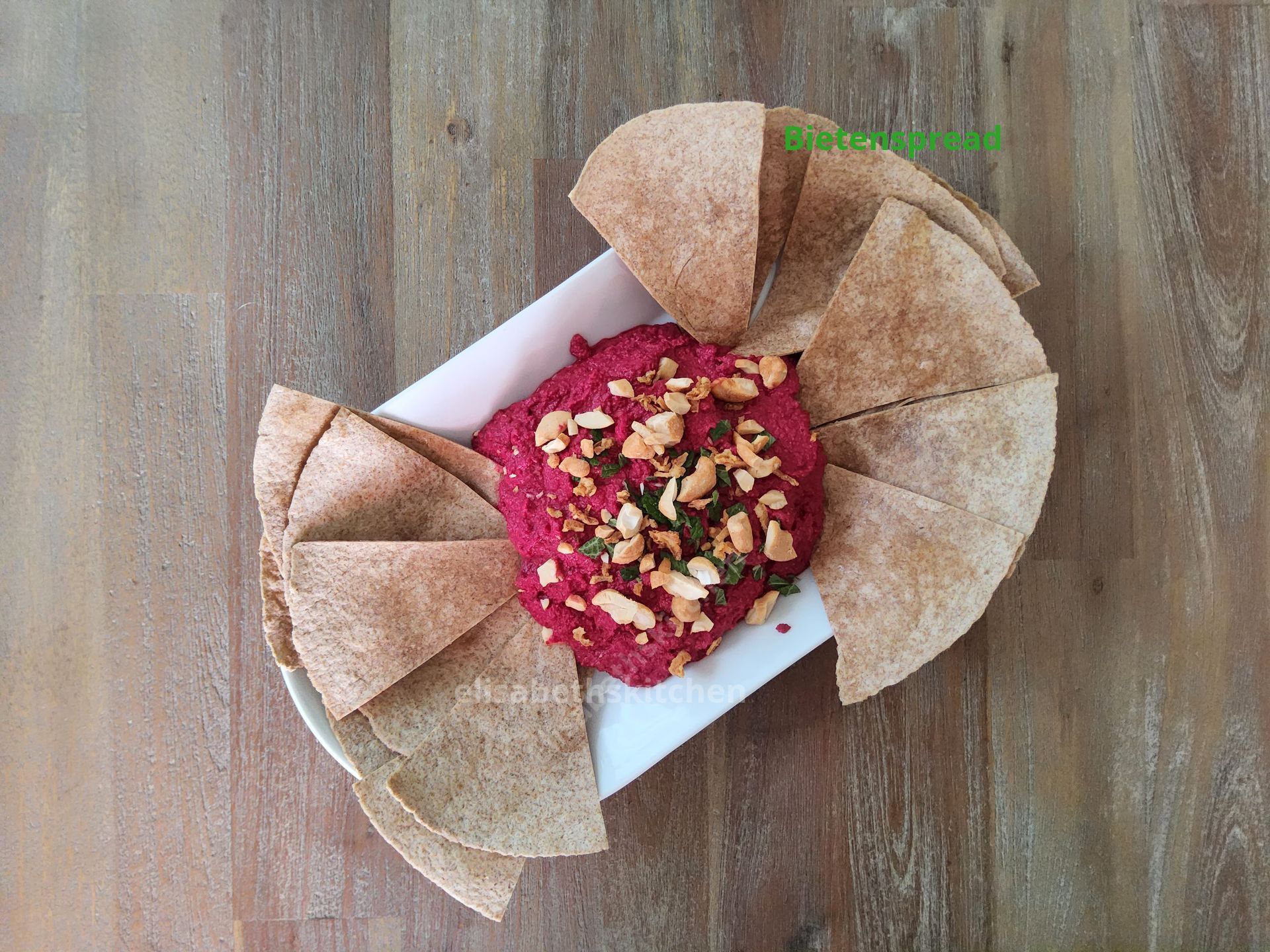 Scroll door voor het recept Bietenhummus met pitachips op een wit bord, met een houten achtergrond.