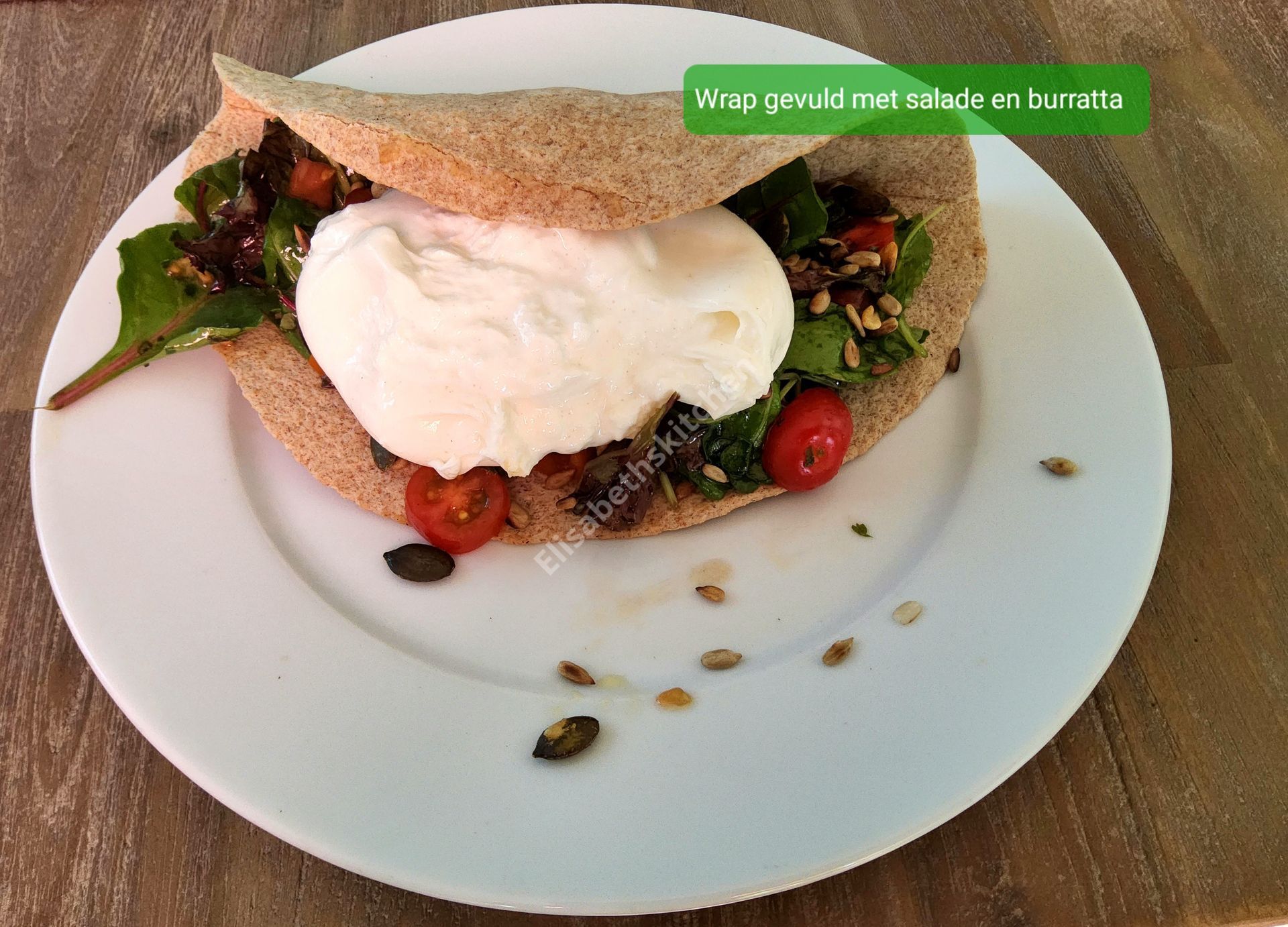 Burrata en salade wrap op een wit bord met verspreide zaden; groene tekst.