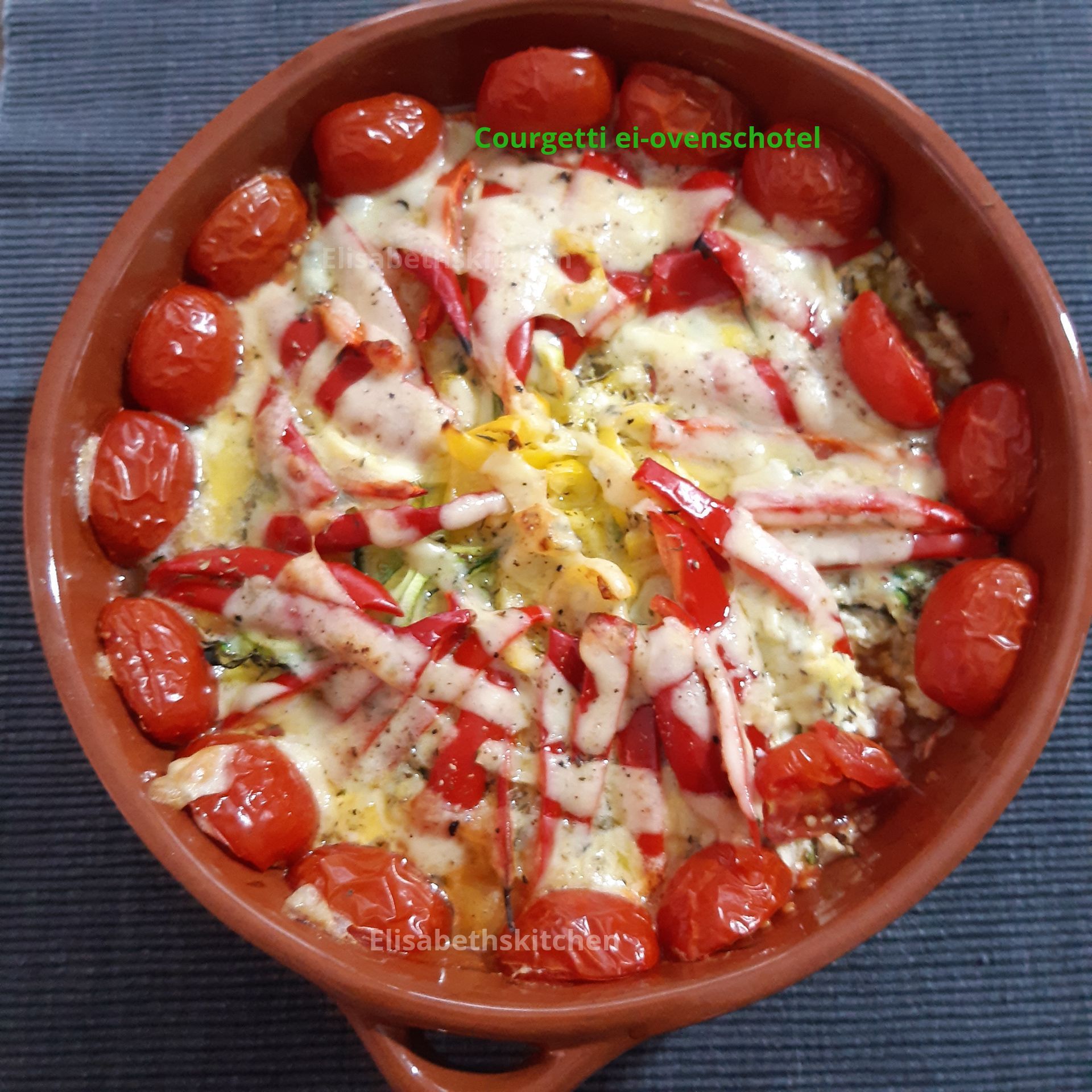 Gebakken courgette met geroosterde tomaten en kaas in een terracotta schaal.