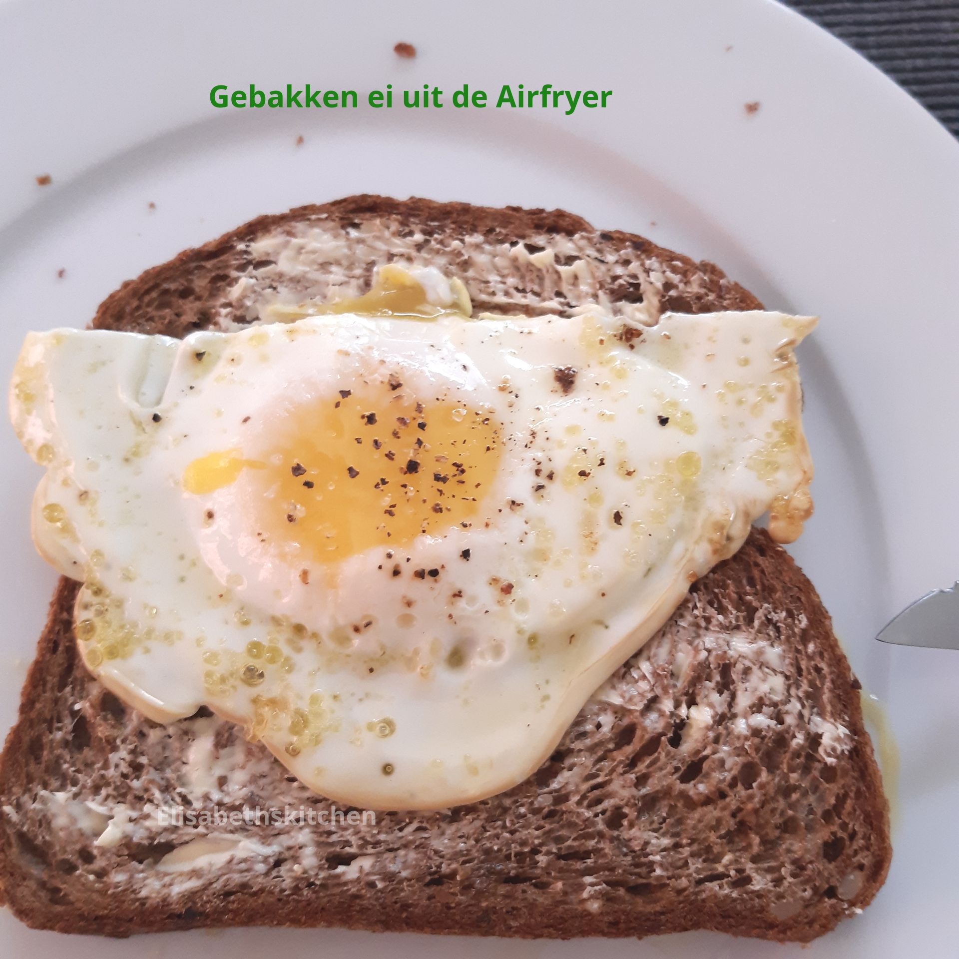 Gebakken ei op donker brood, gekruid met peper. Tekst: 