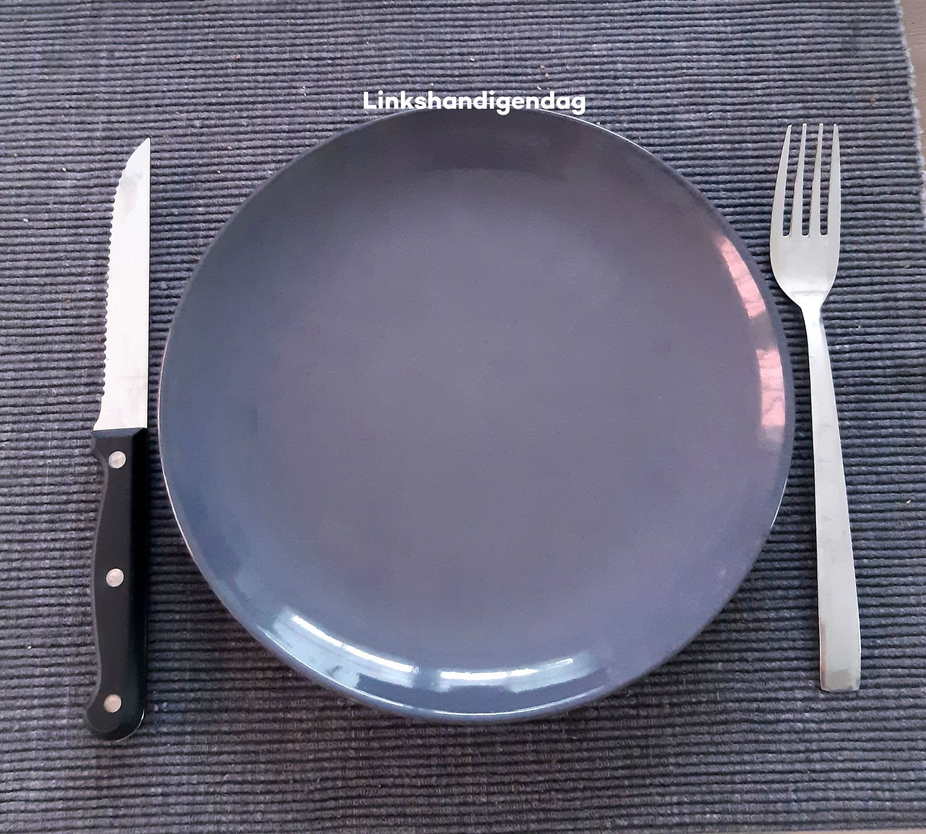 Mes en vork aan weerszijden van een grijs bord op een donkergrijze placemat.