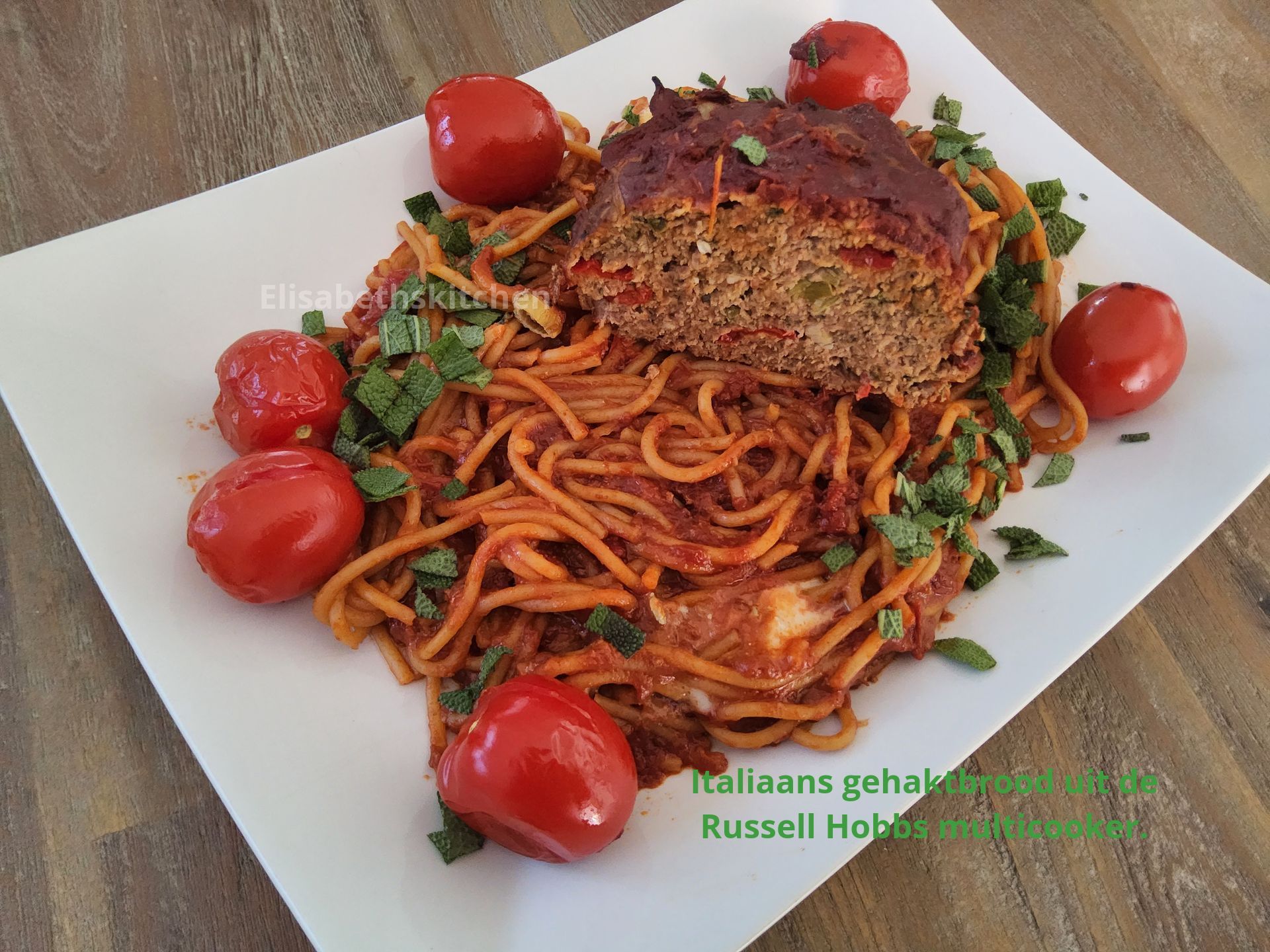 Gehaktbrood met spaghetti, tomaten en basilicum op een wit vierkant bord.