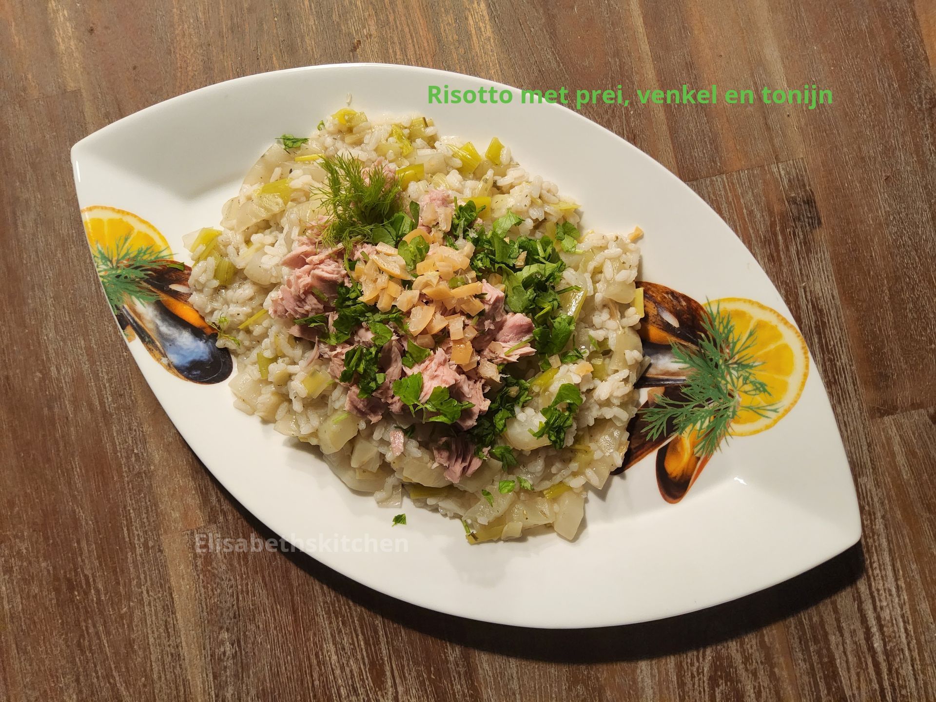 Risotto met prei, tonijn en garnering op een ovaal bord, met schijfjes citroen en mosselen.