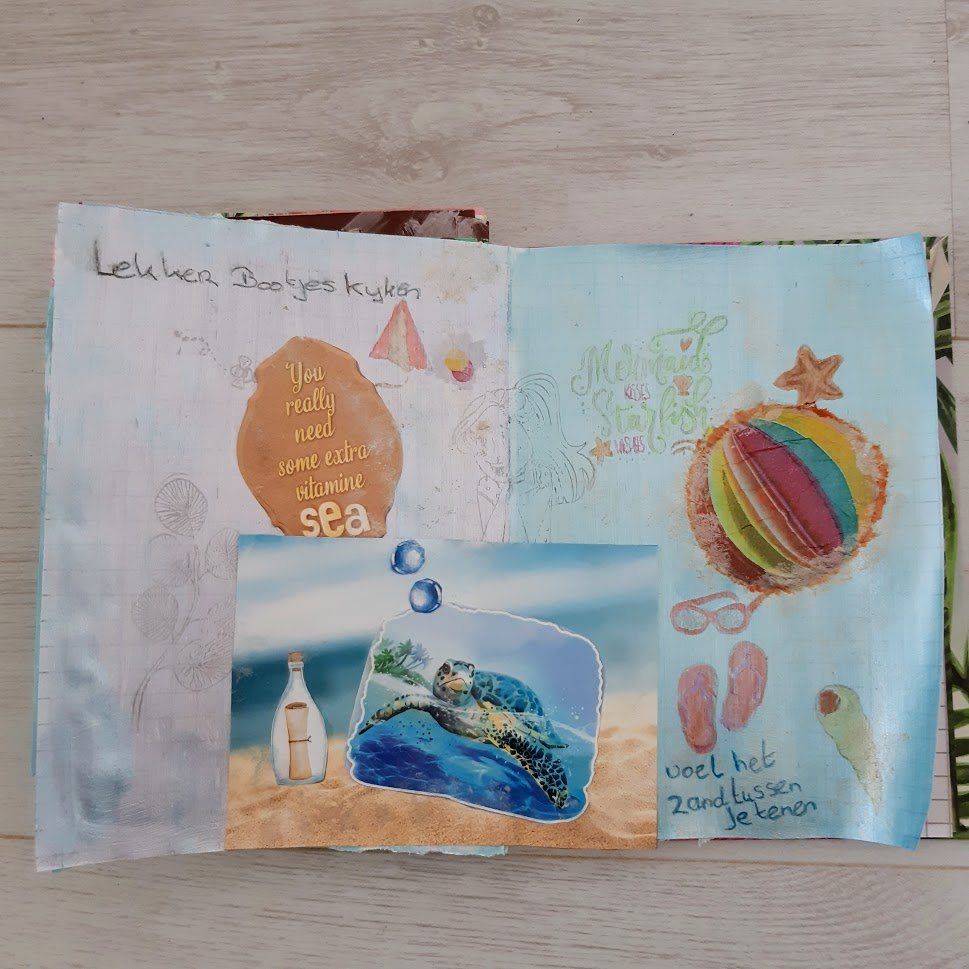 Open pagina's van een plakboek met tekeningen, een foto en tekst met een strandthema.