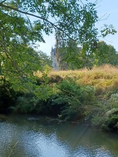Een rivier stroomt langs een met gras begroeide heuvel, met in de verte een kasteel onder een zonnige hemel.