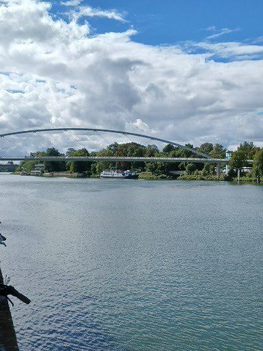Rivier met brug, bewolkte lucht. Boot bij groene bomen en witte brugpijlers.